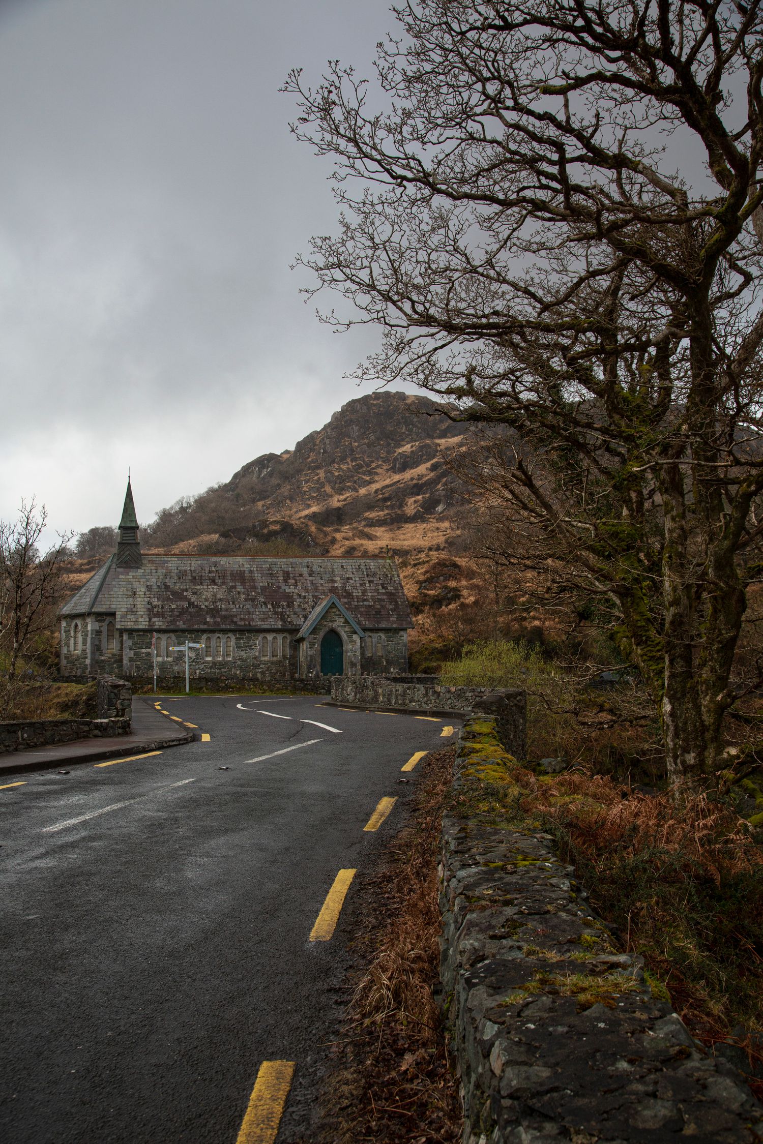 Stone buildings line a curved mountain road with yellow center lines under overcast skies.
