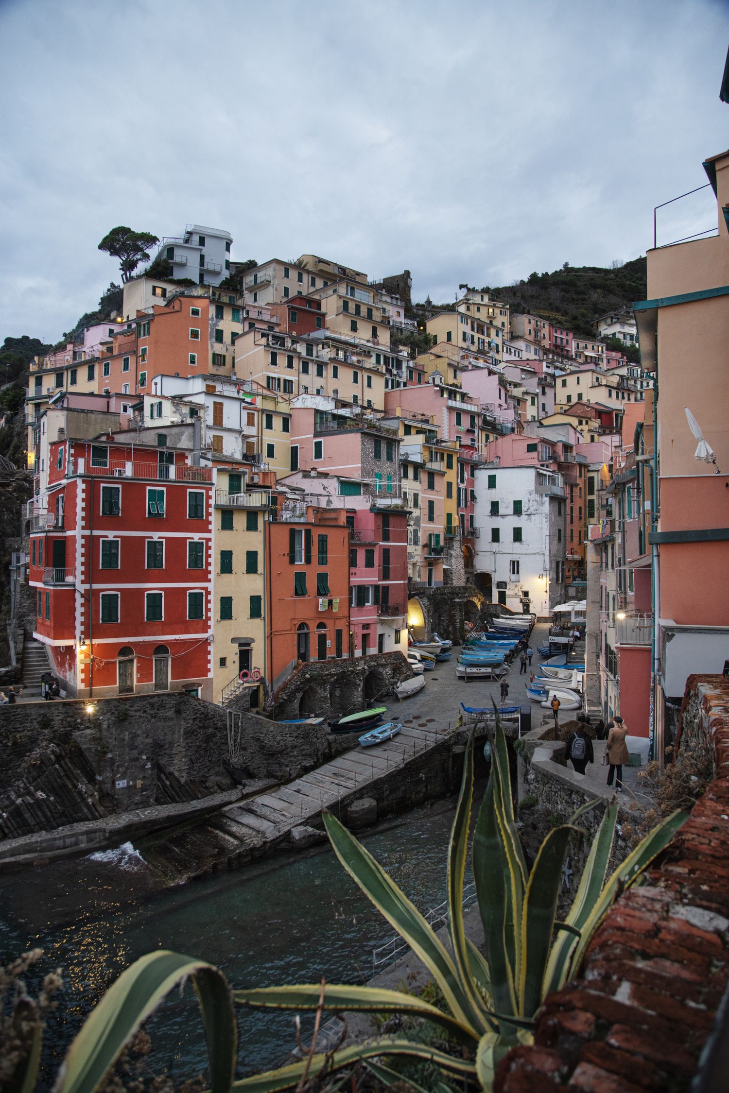Colorful buildings cascading down a hillside in Riomaggiore, Cinque Terre, Italy, at dusk with a small harbor canal.