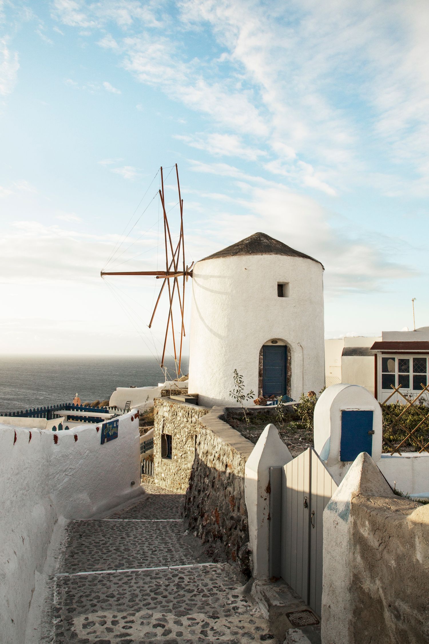 Iconic white windmill with wooden blades stands along a cobblestone path overlooking the Mediterranean Sea.