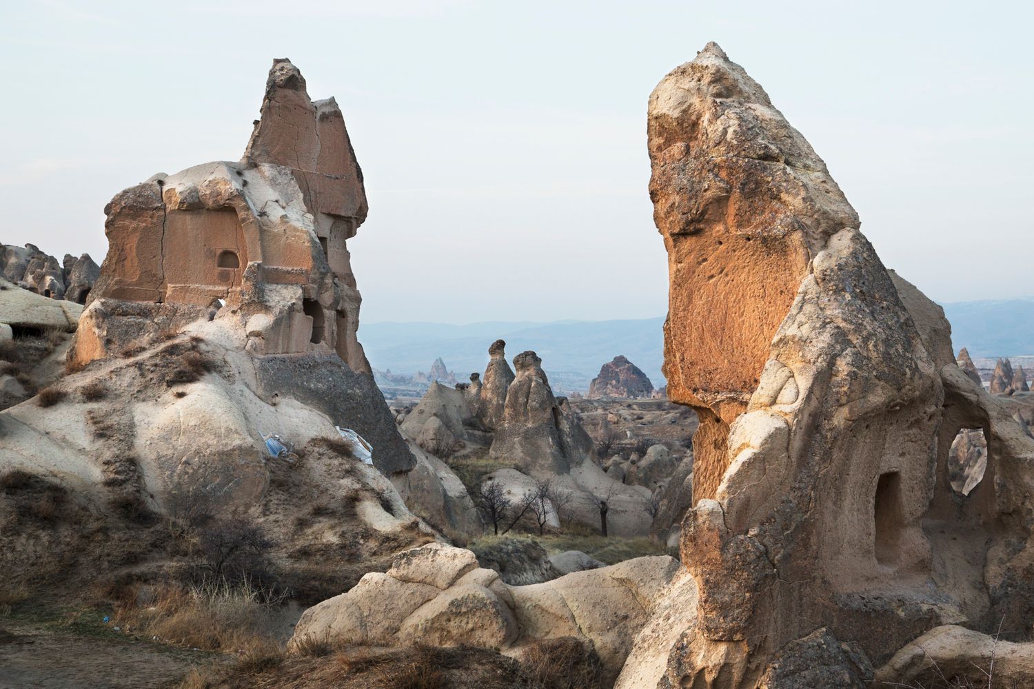 Unique rock formations and carved cave houses stand against a bright sky in the Turkish landscape.