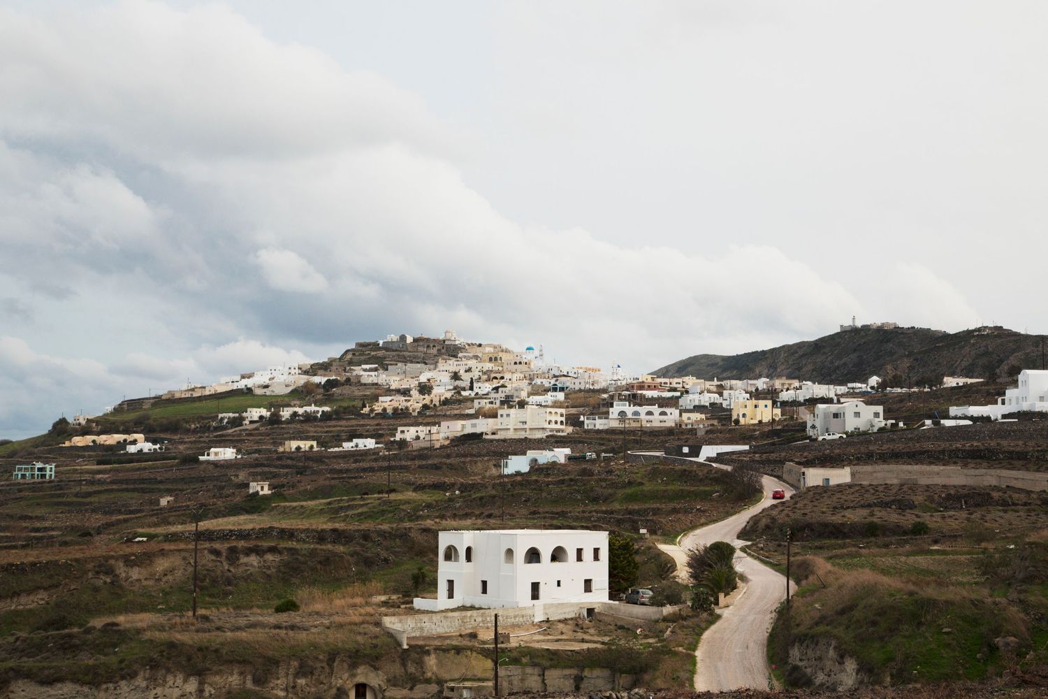 Panoramic view of white buildings dotting a hillside landscape under cloudy skies.