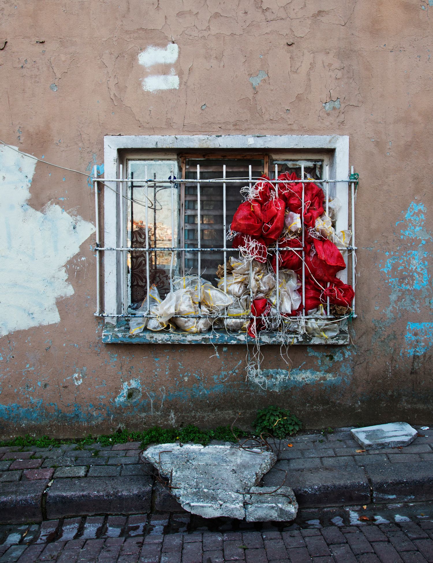 Red flowers blooming in window boxes along a weathered stone wall with peeling paint.