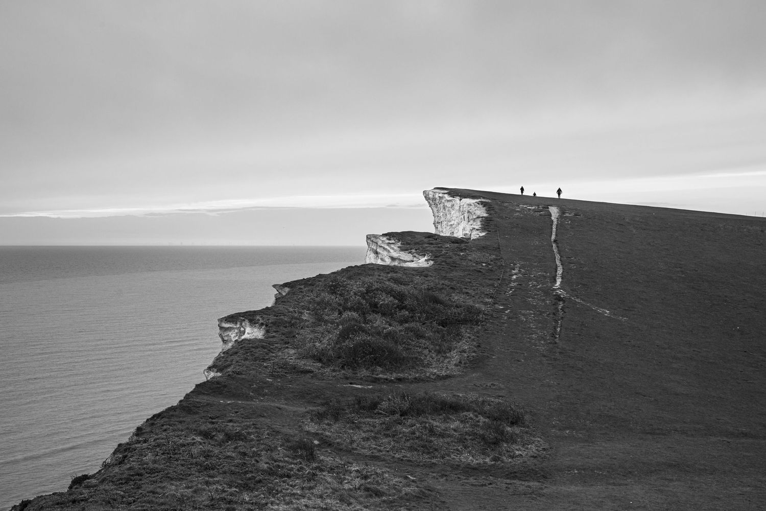 Dramatic black and white panoramic view of coastal cliffs against a moody sky.