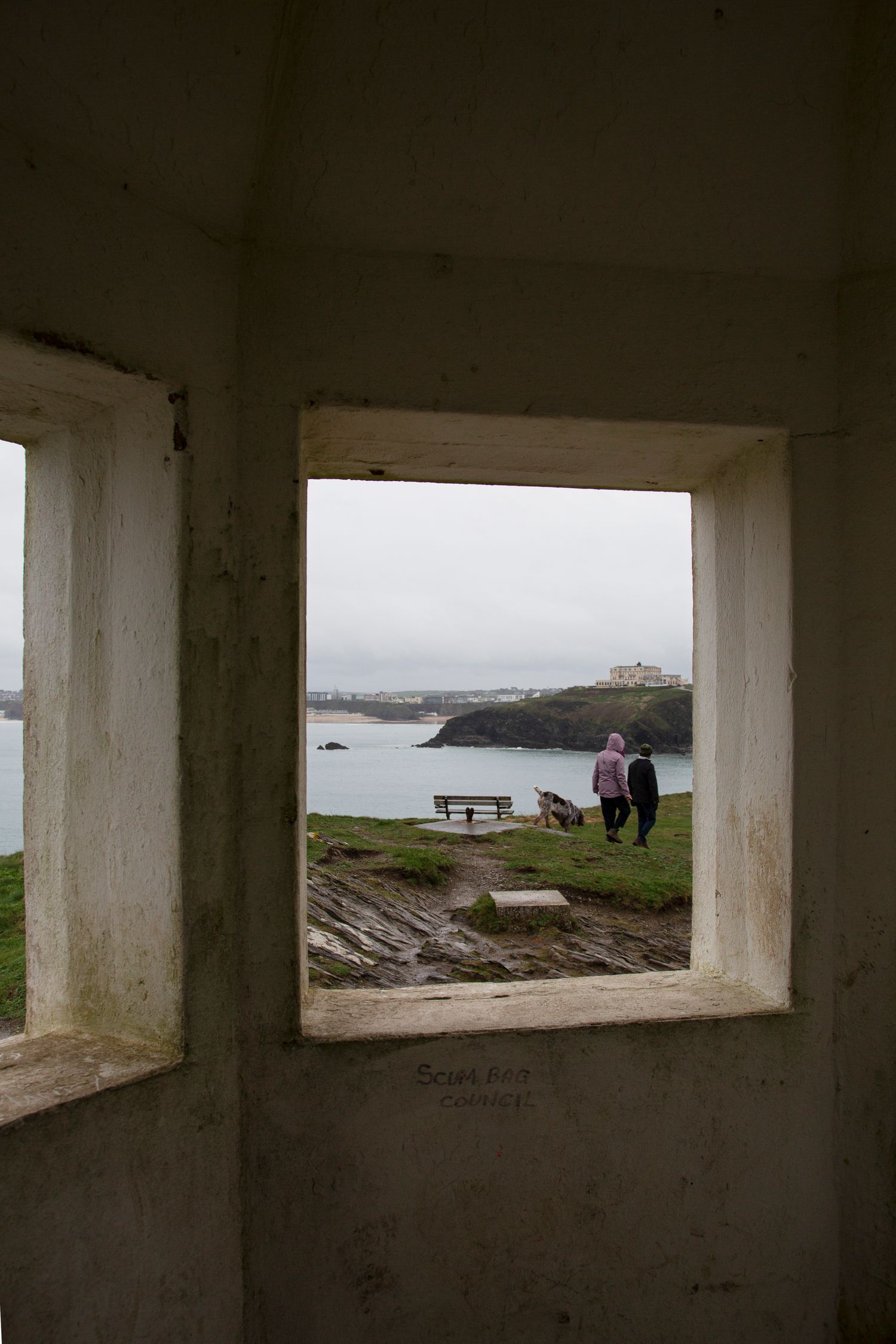 View through concrete window frame of coastal scenery and bench overlook.