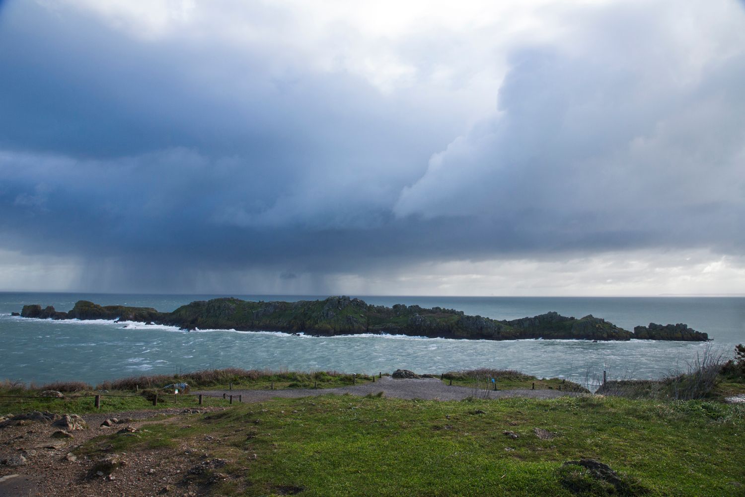 Dramatic stormy skies over a rocky coastline with scattered islands visible in the distance.