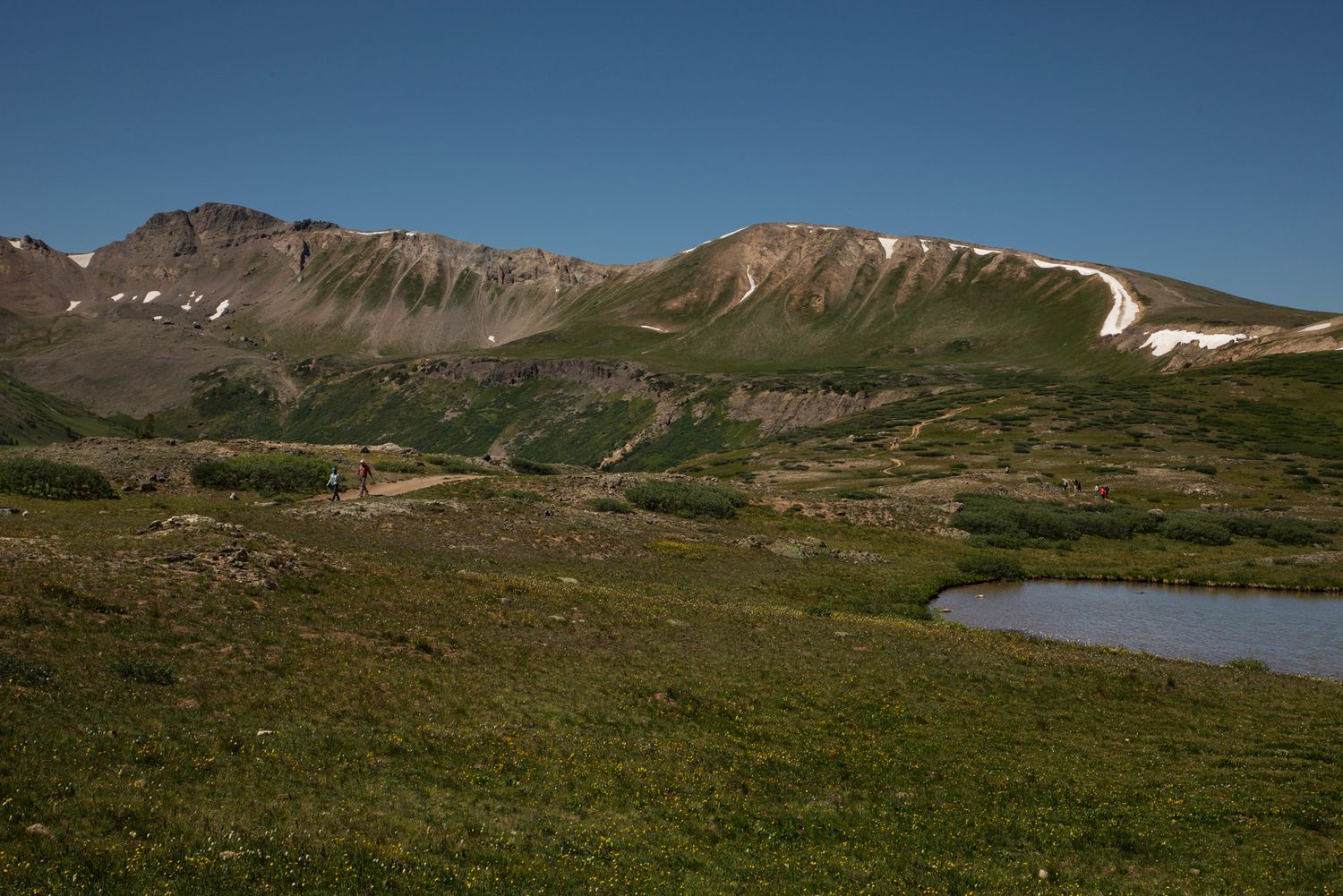Scenic mountain landscape with snow patches and green alpine meadows under a deep blue summer sky.