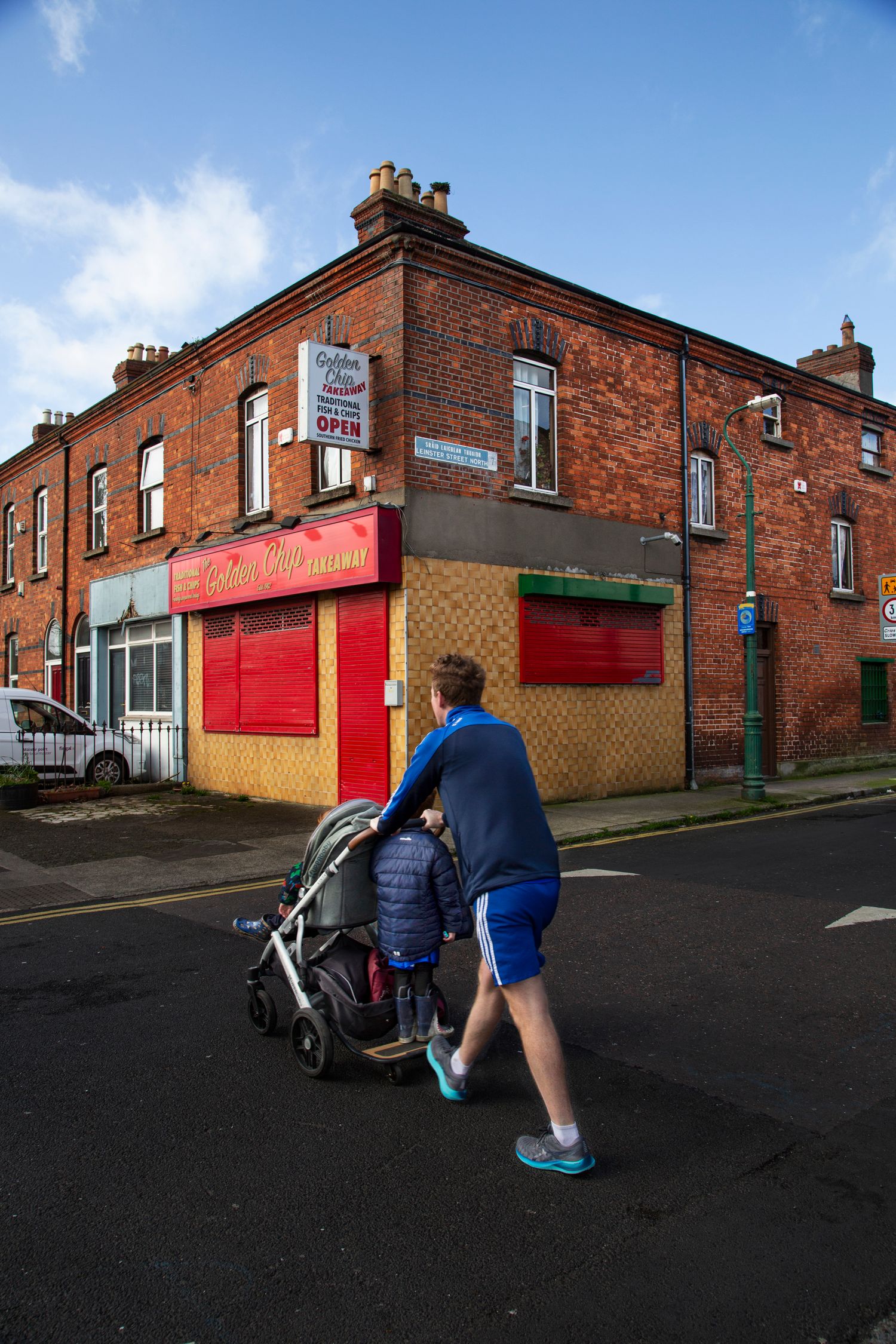 People walking past red brick buildings on a residential street corner.