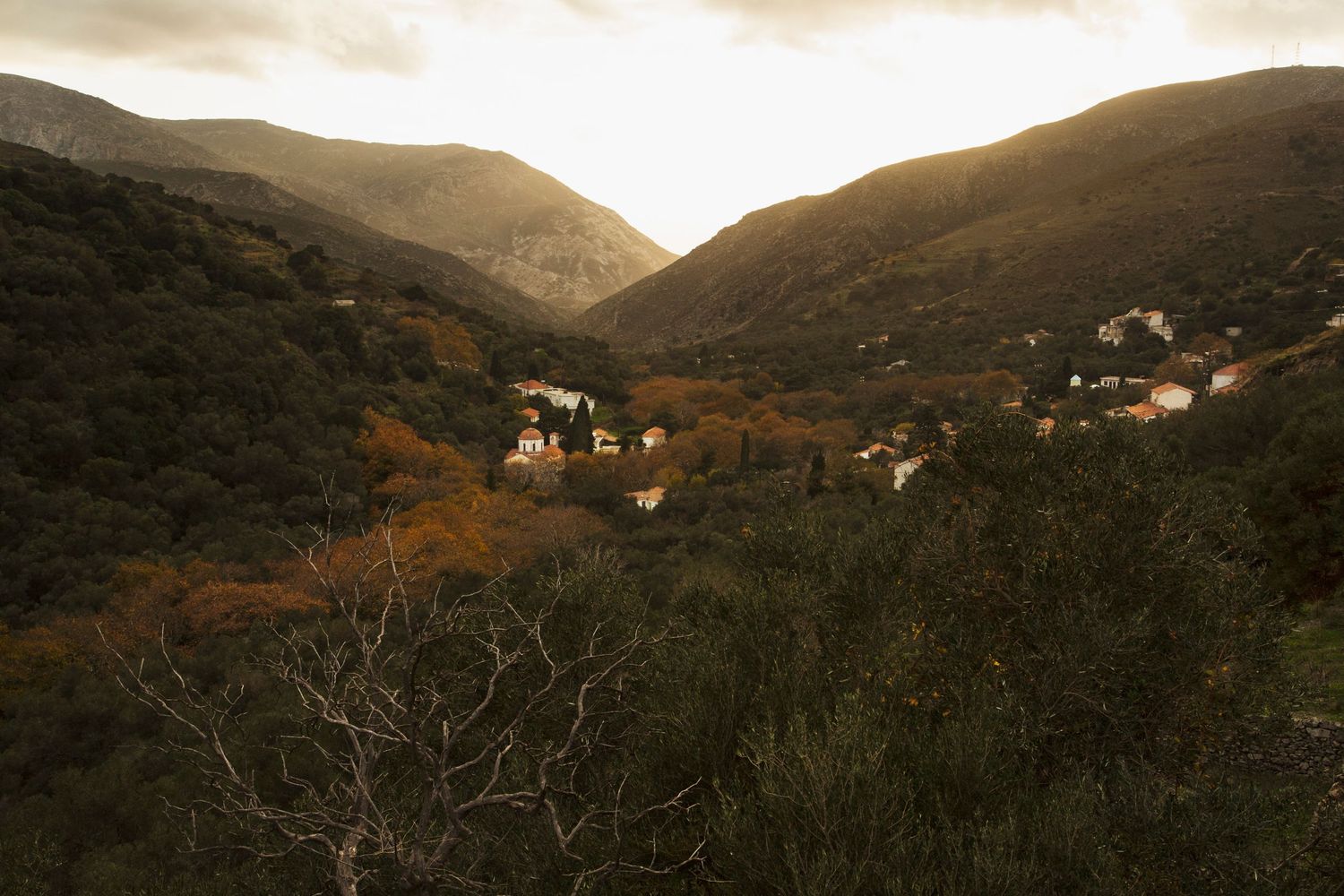 Mountainous landscape at sunset with scattered houses in valley below.