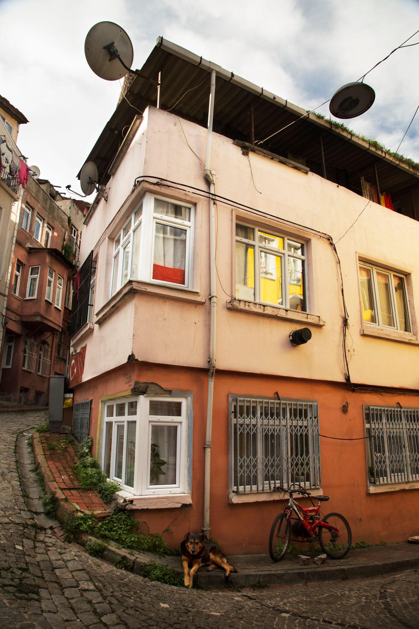 Corner building with bay windows, satellite dishes and red bicycle on steep cobblestone street.