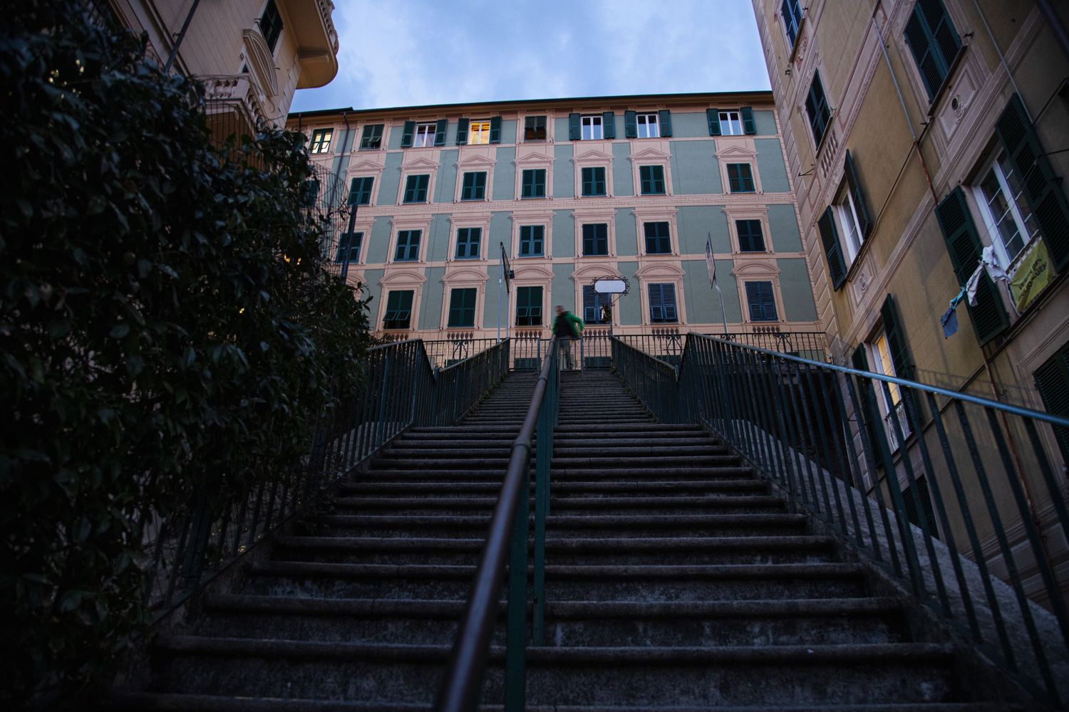 Stone staircase leading to a historic Italian apartment building with green shuttered windows at dusk.