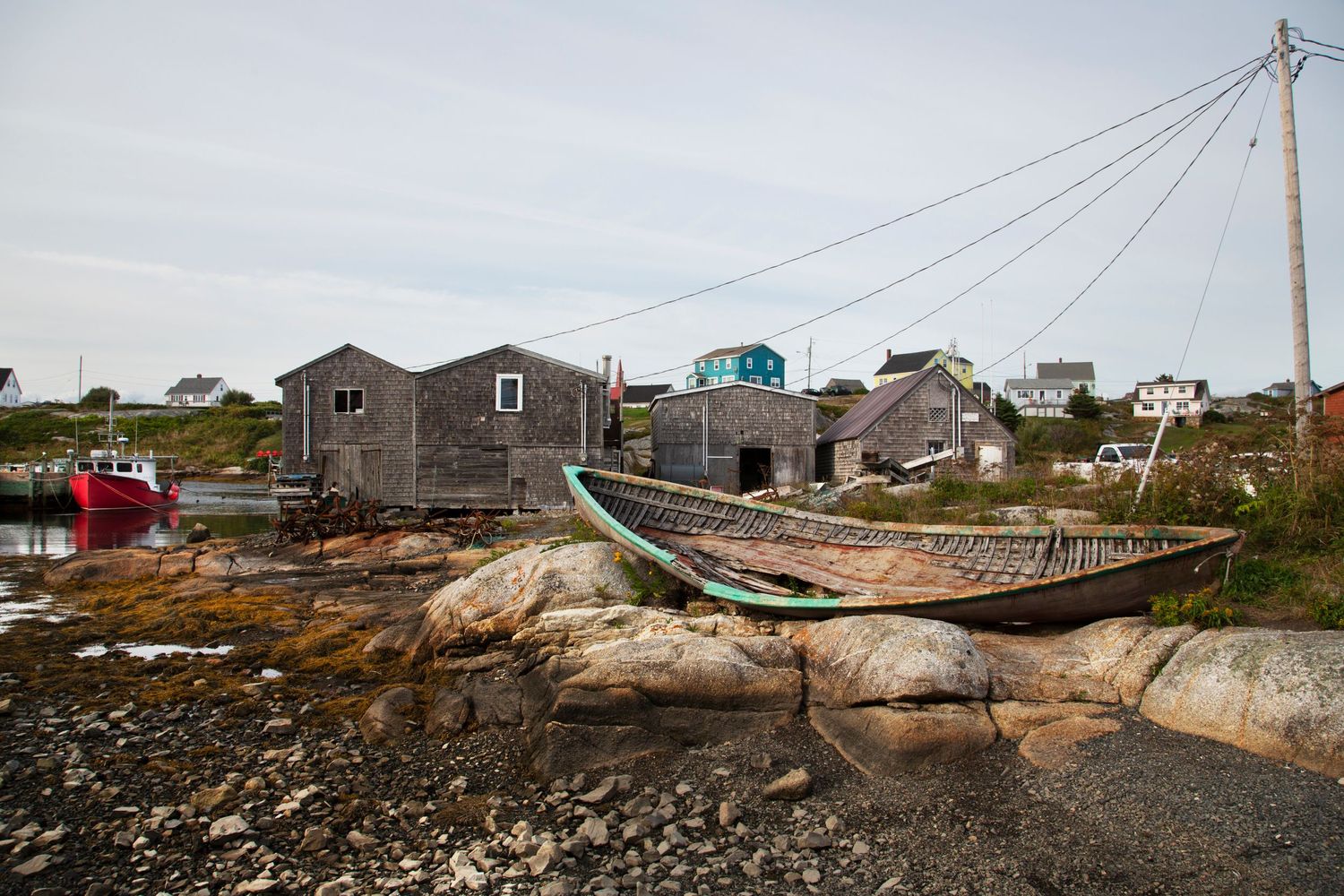 Rustic fishing village with wooden buildings and boats on rocky shore during low tide.