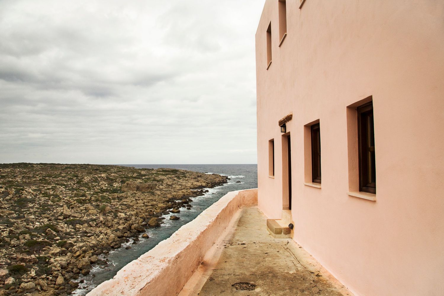 Peach-colored lighthouse building with square windows overlooking coastal landscape.