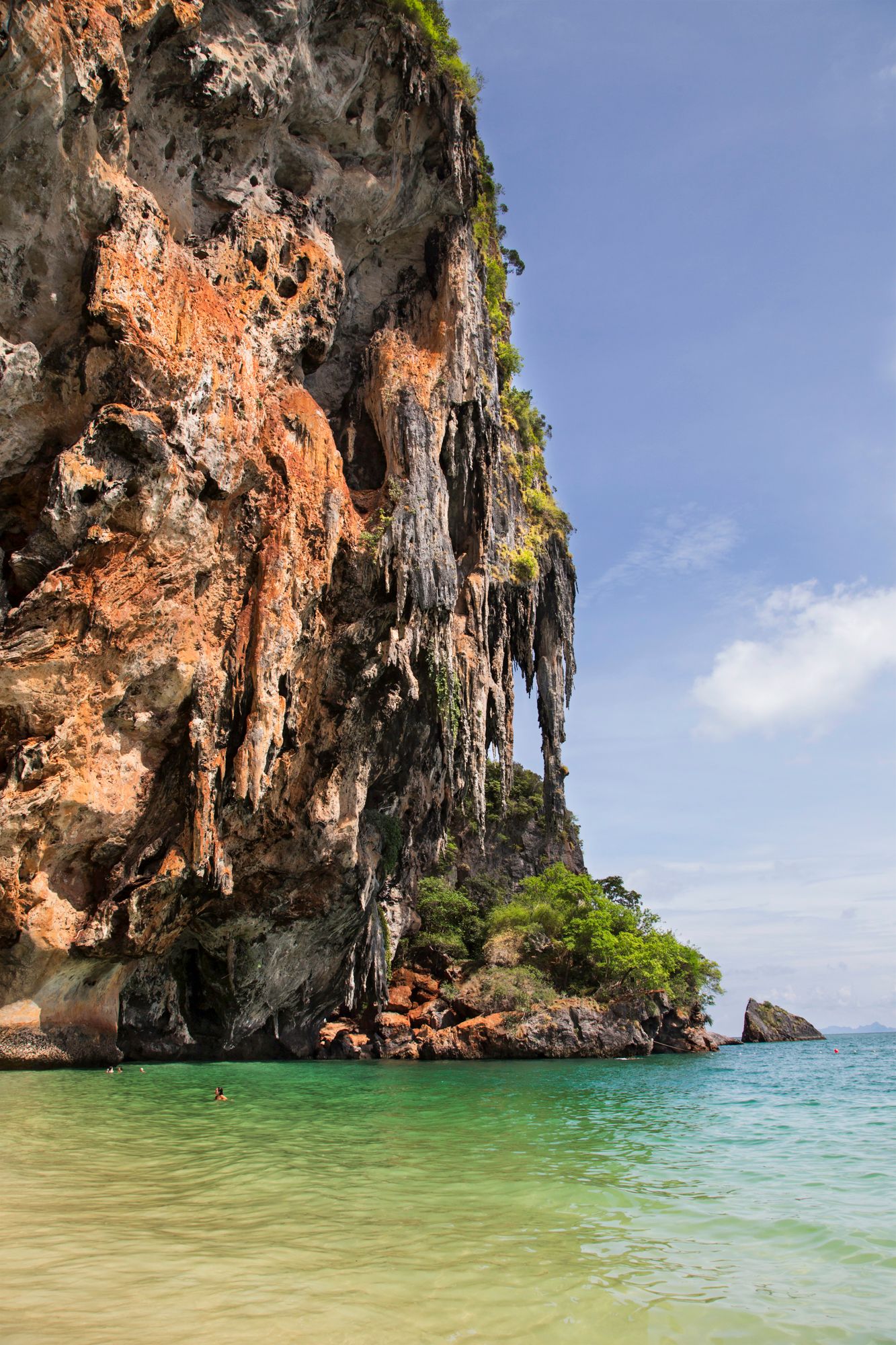 Dramatic limestone cliffs rise from turquoise waters along a tropical coastline.