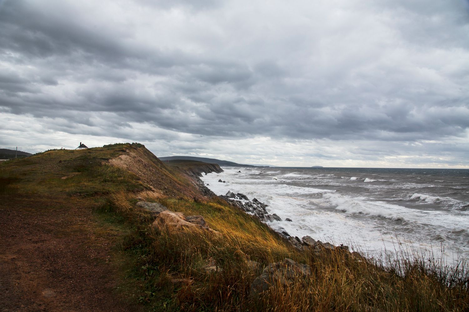 Dramatic stormy coastline with steep cliffs and crashing waves under dark cloudy skies.