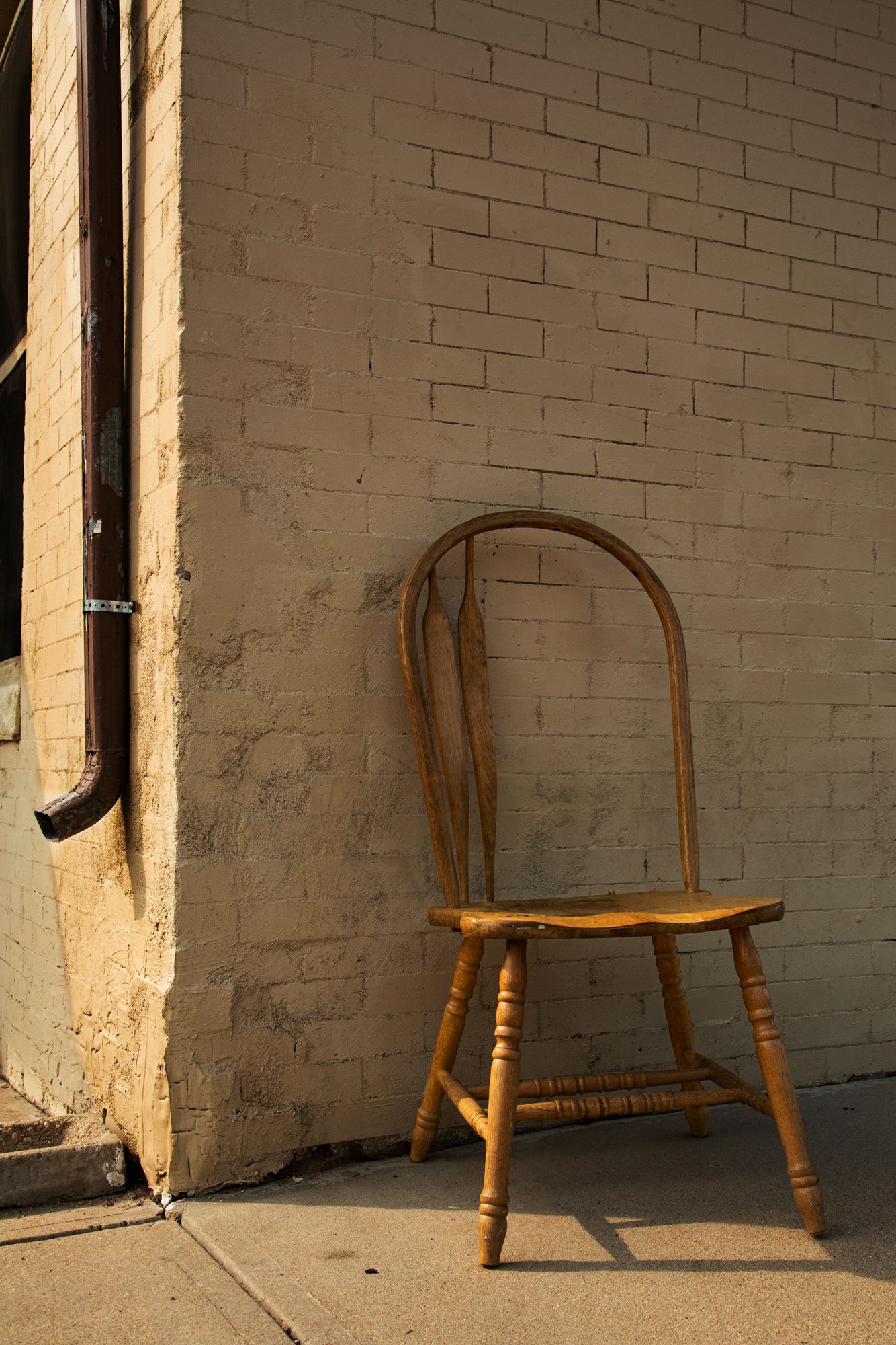Wooden Windsor chair positioned against a white painted brick wall in varying lighting conditions.