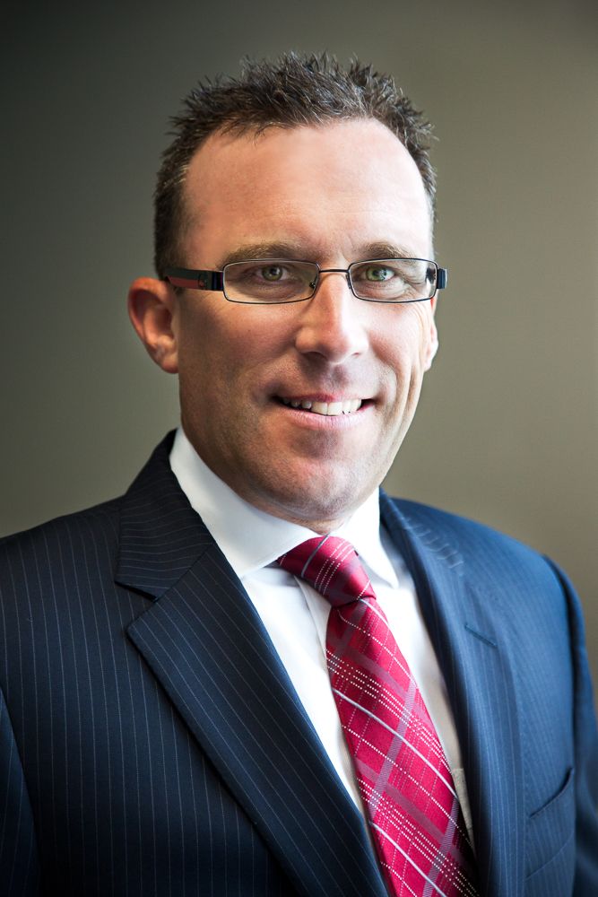 Professional wearing a pinstriped navy suit with red tie looking to the side and smiling in a studio setting.