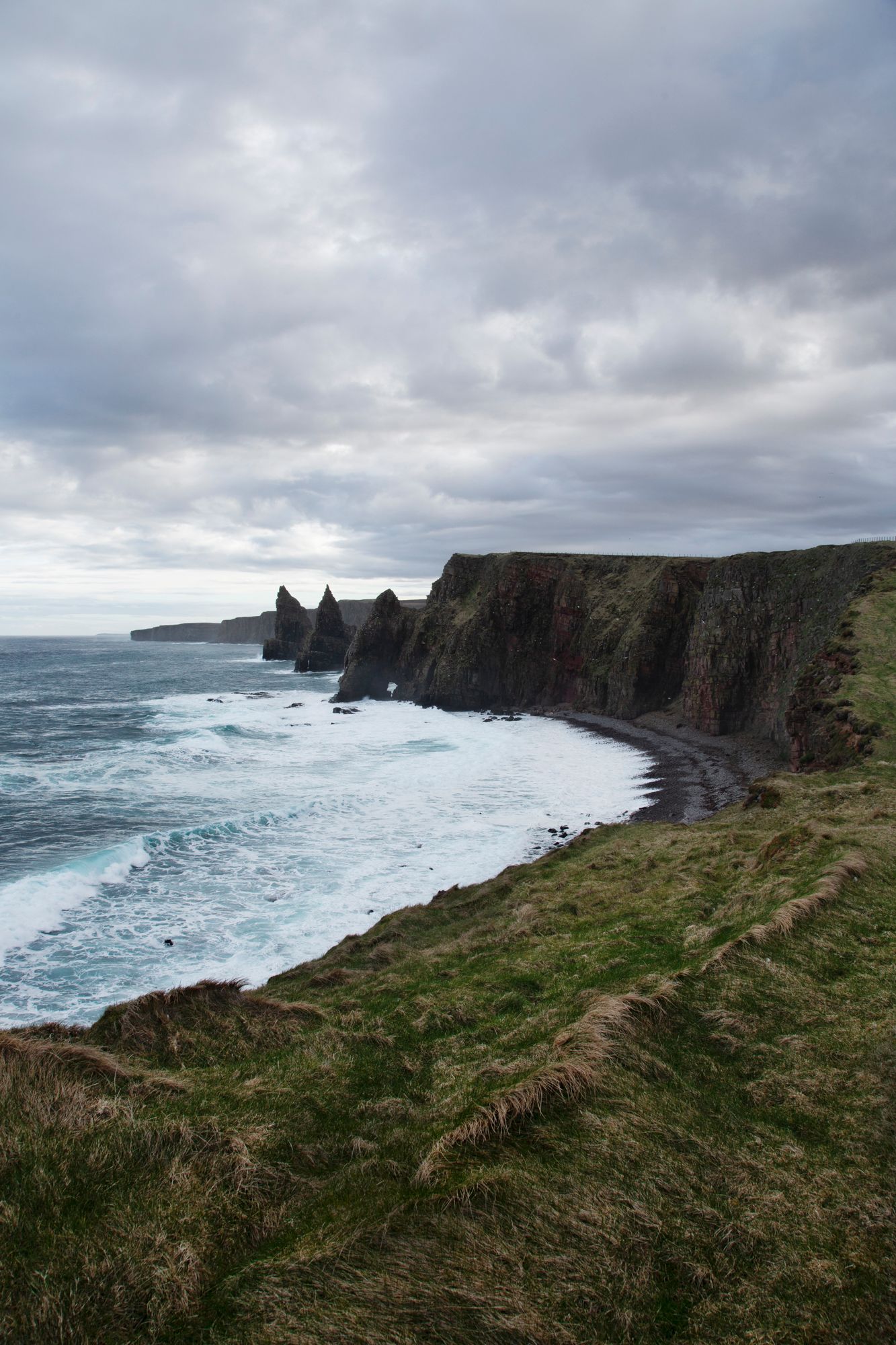 Dramatic coastal landscape showing rugged cliffs and crashing waves along Ireland's Cliffs of Moher on a cloudy day.