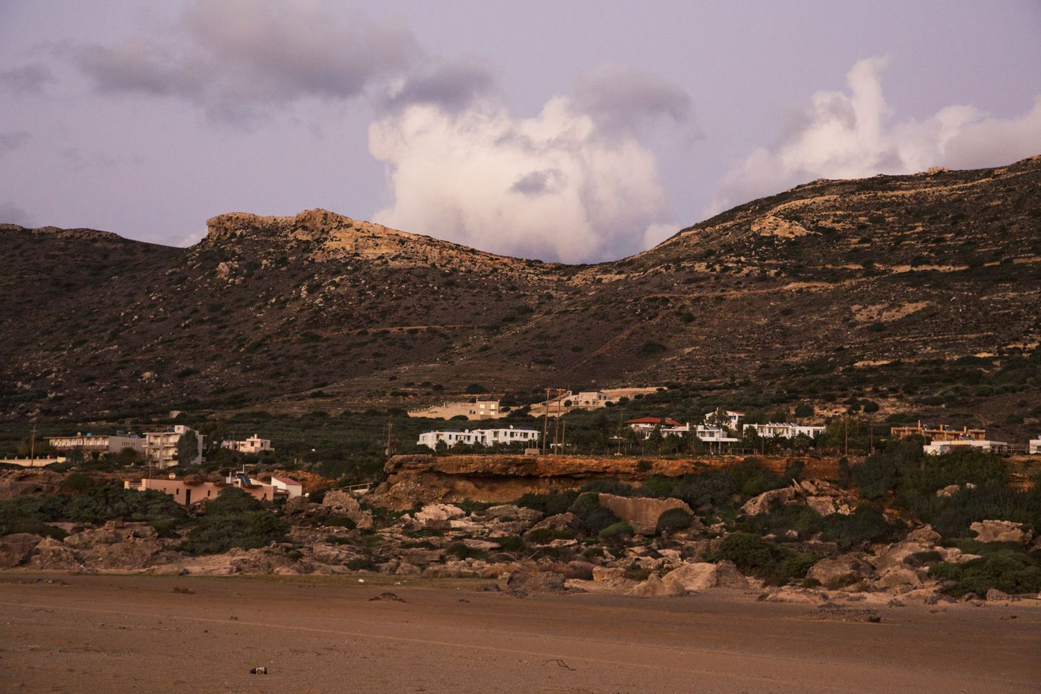 Desert mountain landscape with scattered buildings under a cloudy sky.