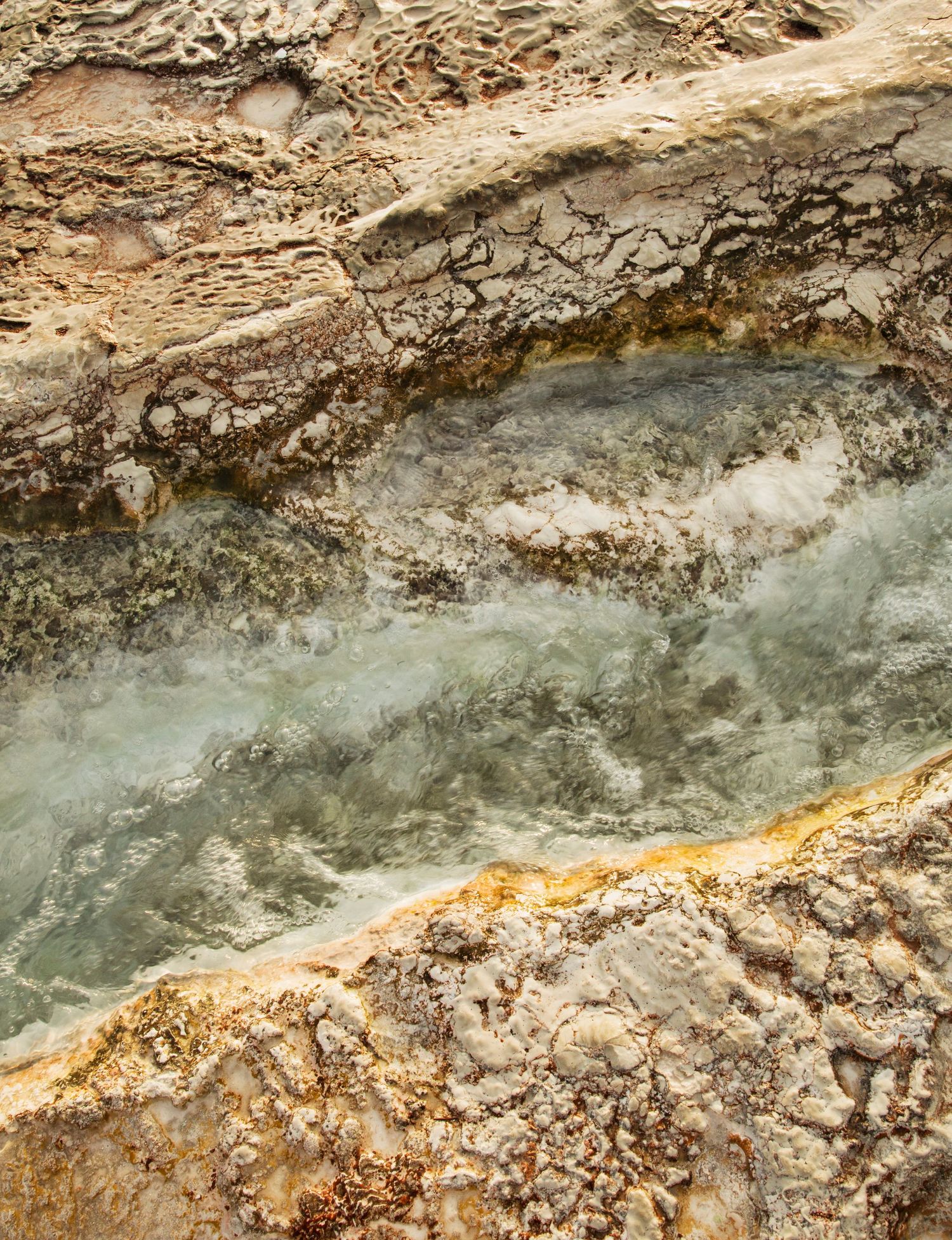 Colorful mineral deposits and steaming water create abstract patterns in a geothermal landscape.