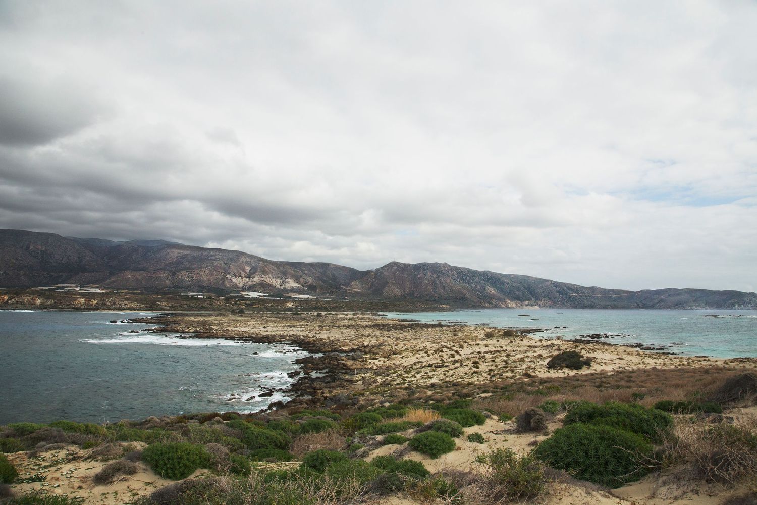 Rocky coastline with mountains and cloudy sky overlooking Mediterranean waters.