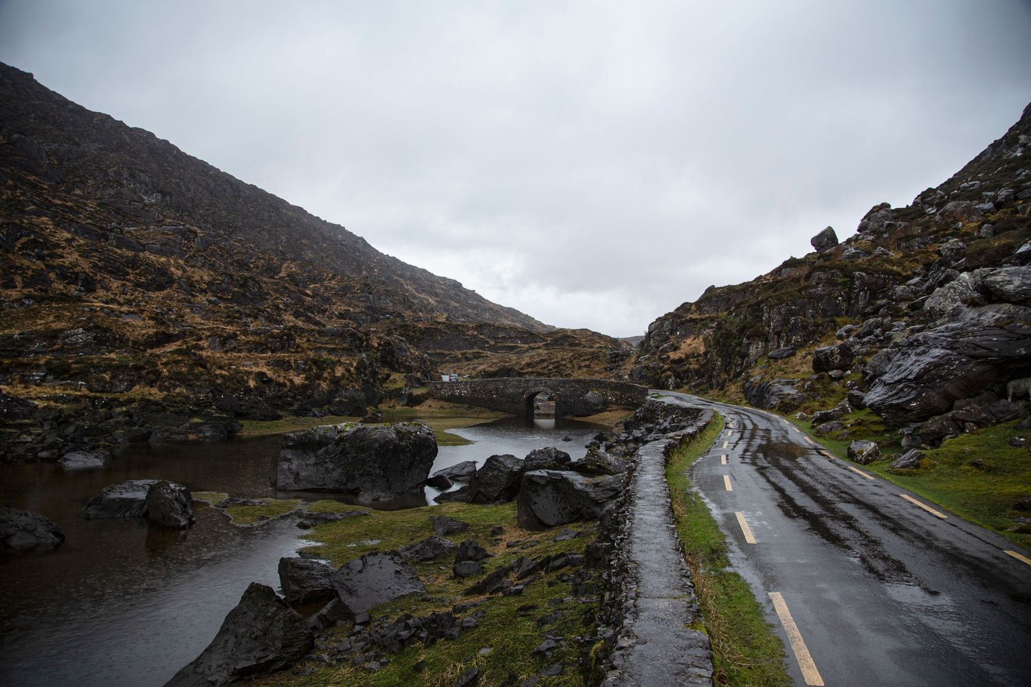 Winding mountain road curves through rugged landscape with dramatic cloudy skies in Ireland.