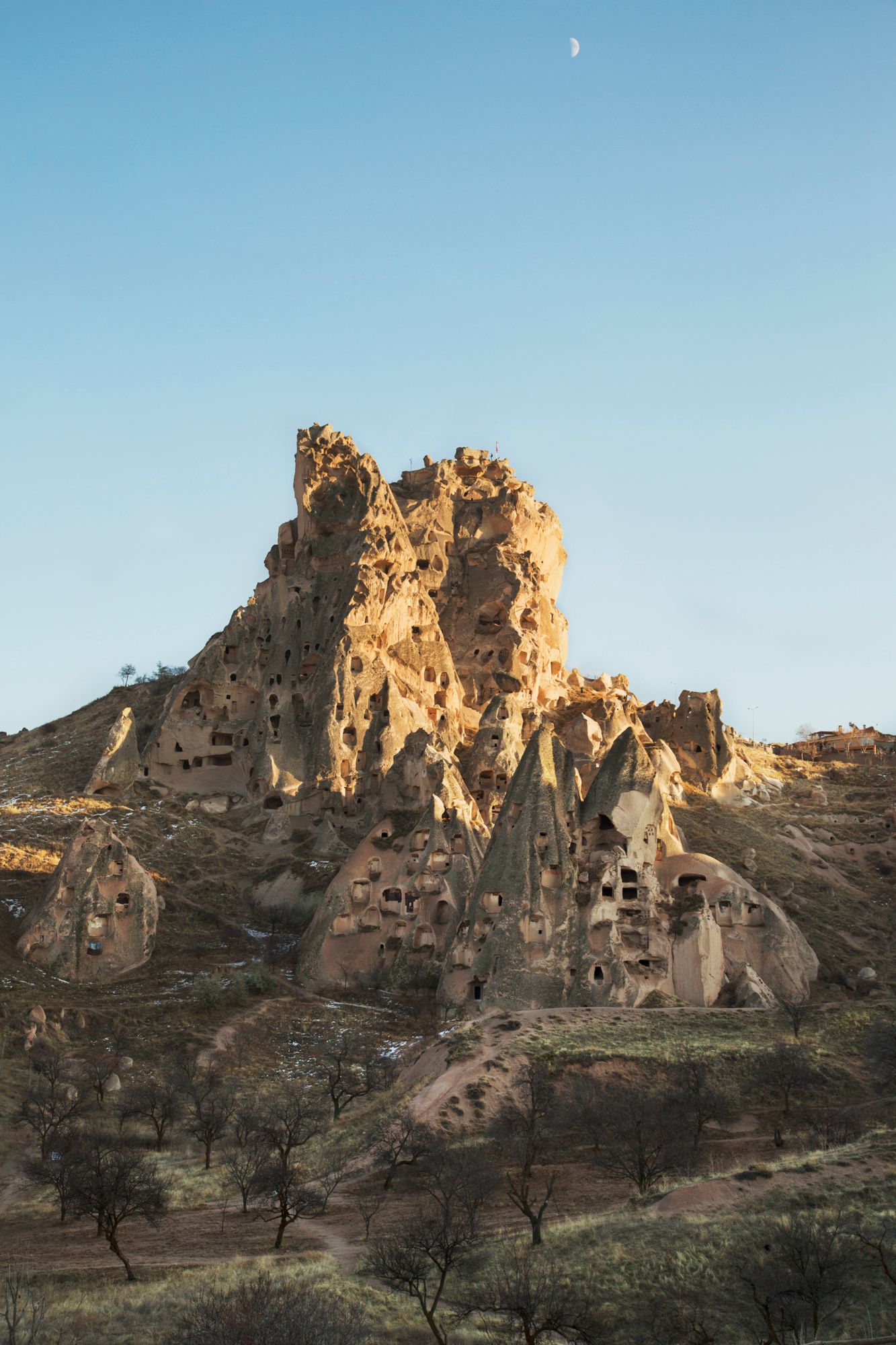 Crescent moon rises over honeycomb-like cave dwellings carved into golden limestone cliffs.