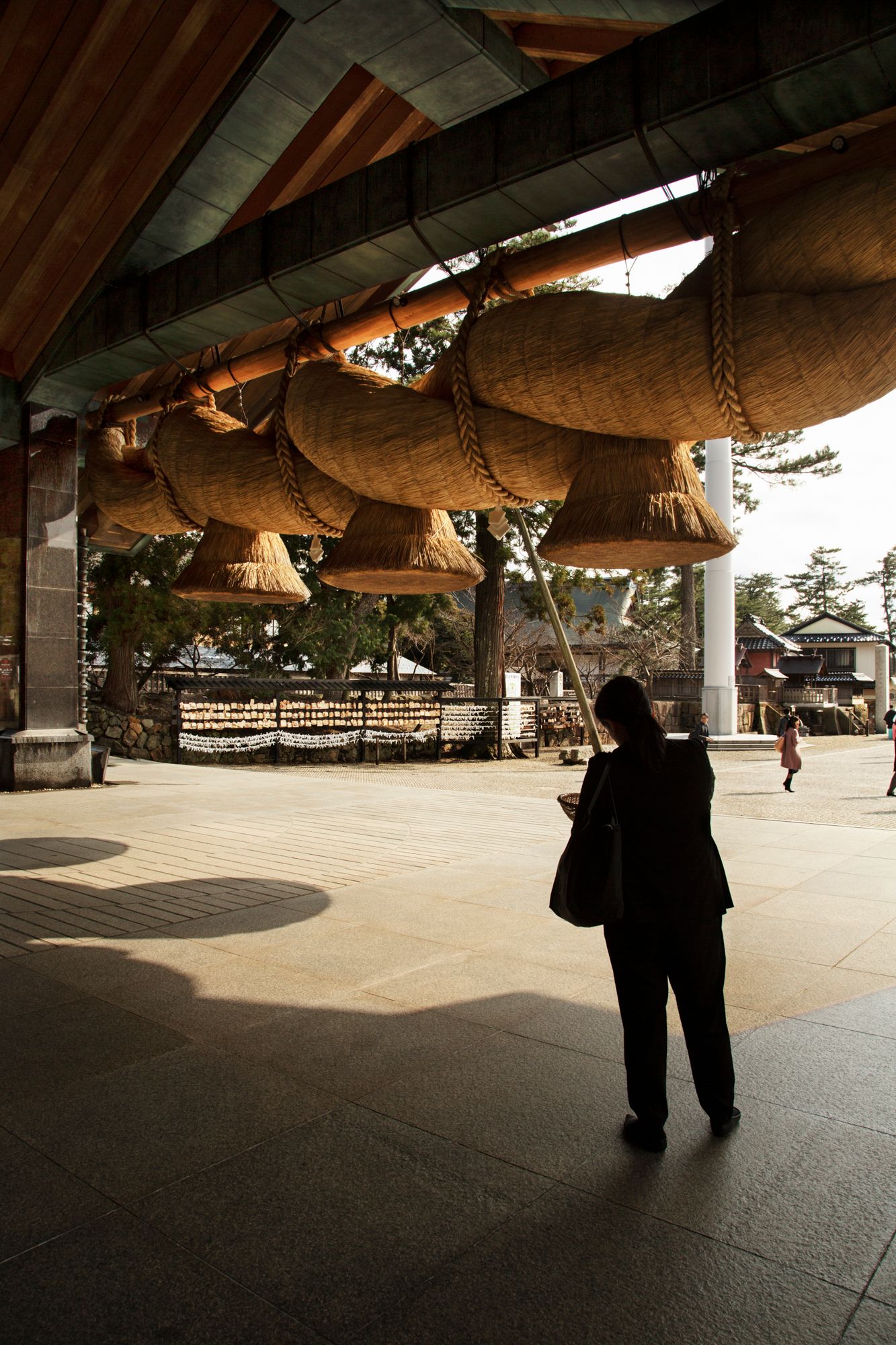 Interior view of covered walkway with hanging wooden beams creating dramatic shadows.
