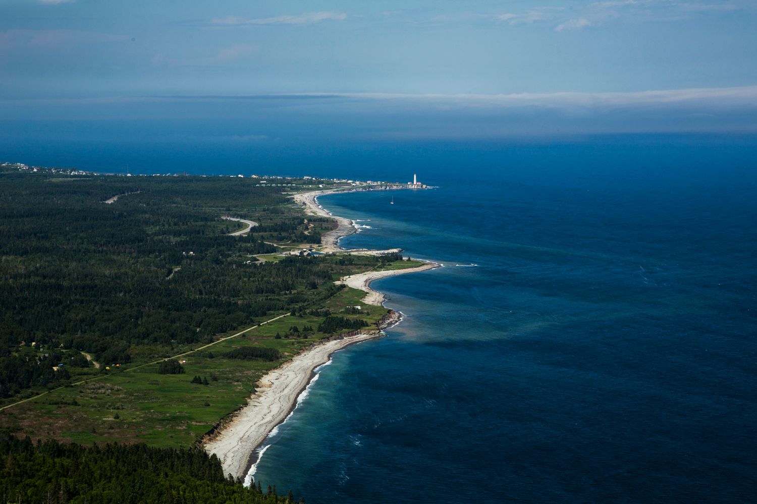 Aerial view of a lighthouse and coastline with sandy beaches stretching along the blue ocean.