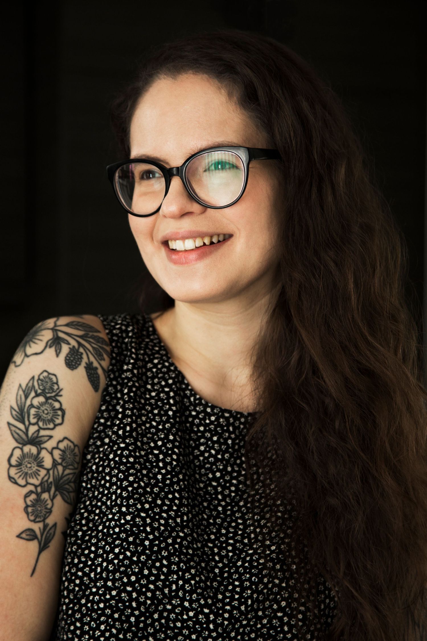 Portrait series showing bright smile and floral tattoo against dark background.
