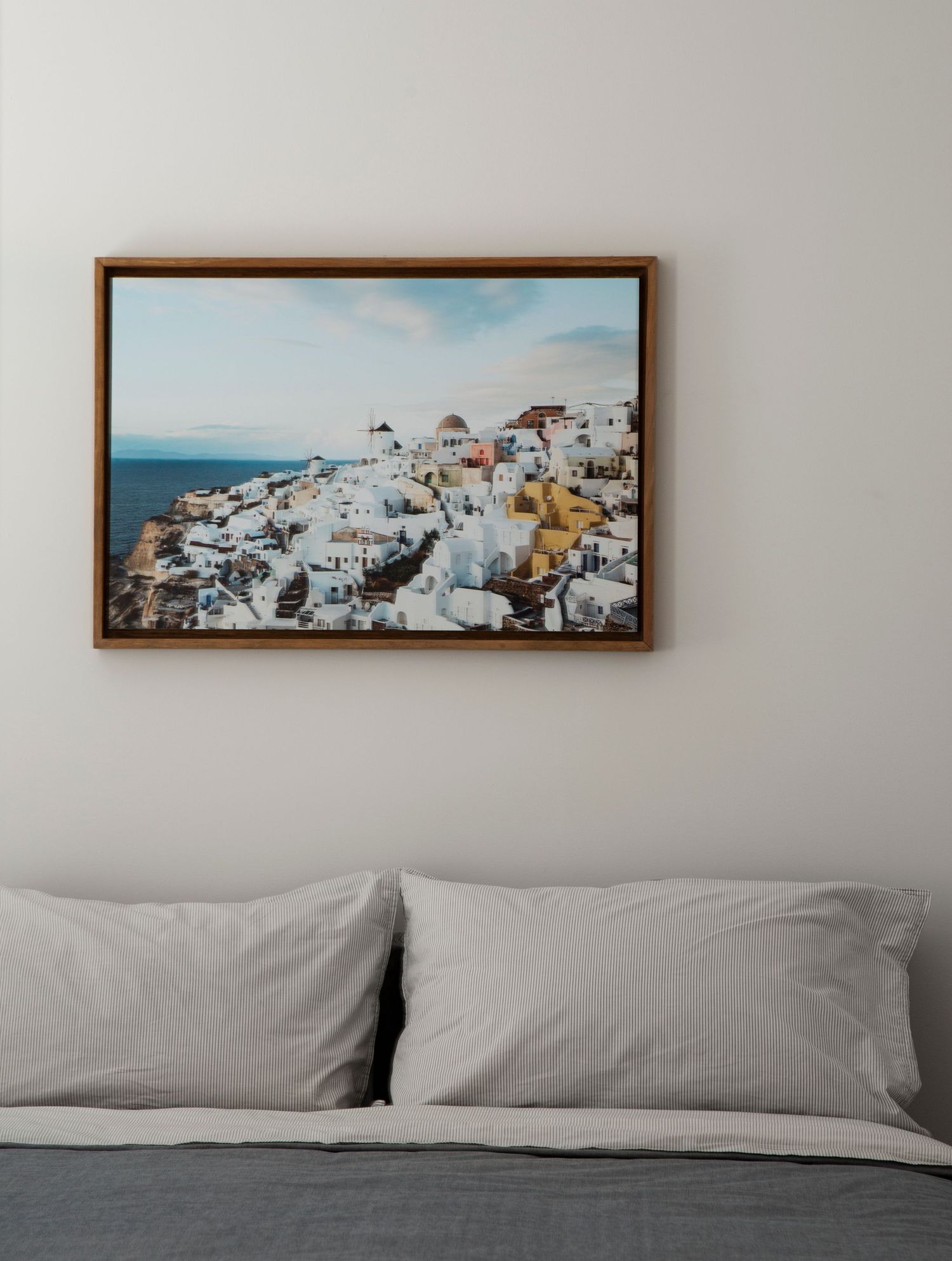 Framed panoramic photograph of white buildings in Santorini mounted above a modern bed.
