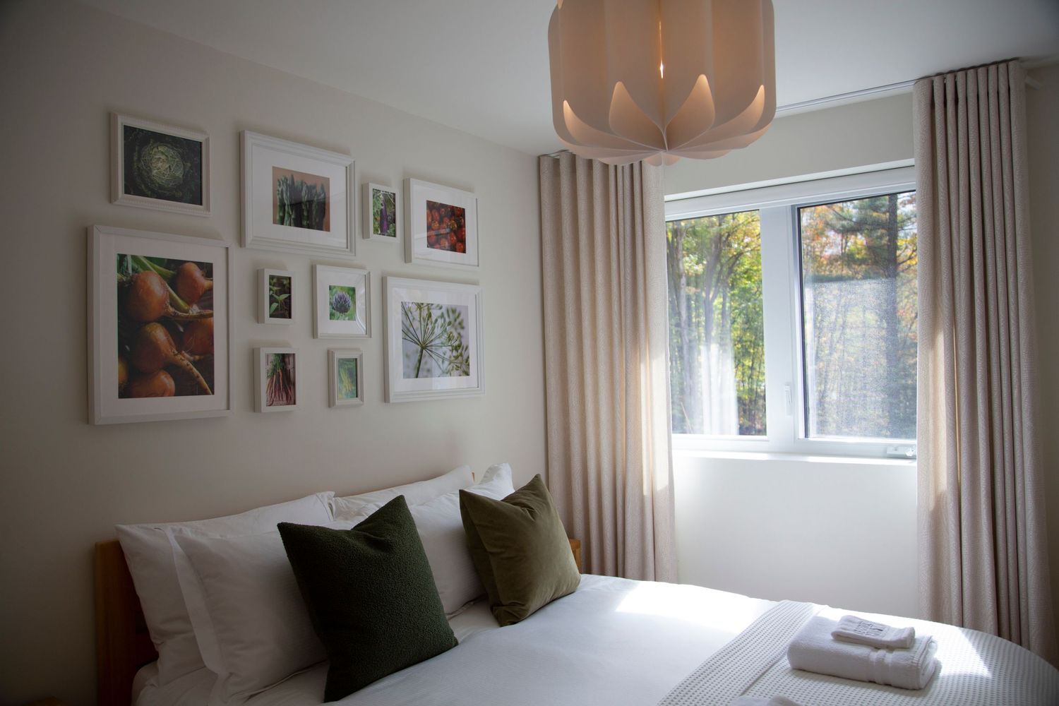 Serene bedroom interior with natural light, soft textiles, and gallery wall of framed artwork.