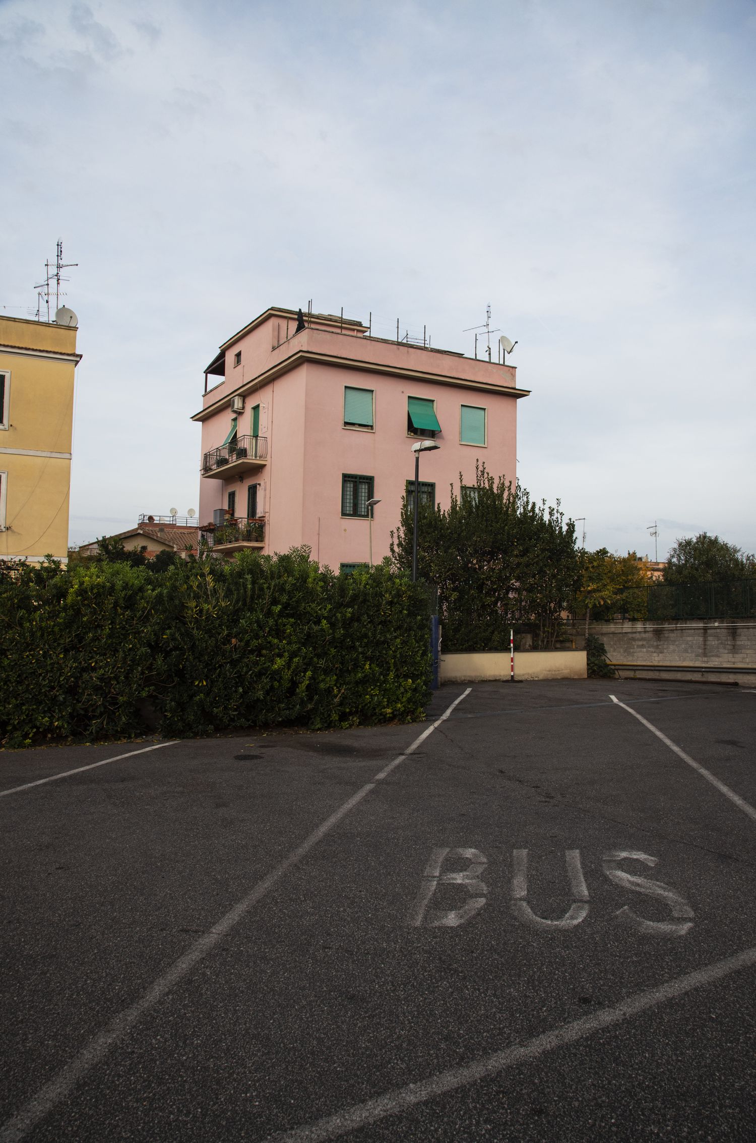 A pink multi-story building behind hedges next to a parking lot with BUS painted on the asphalt.