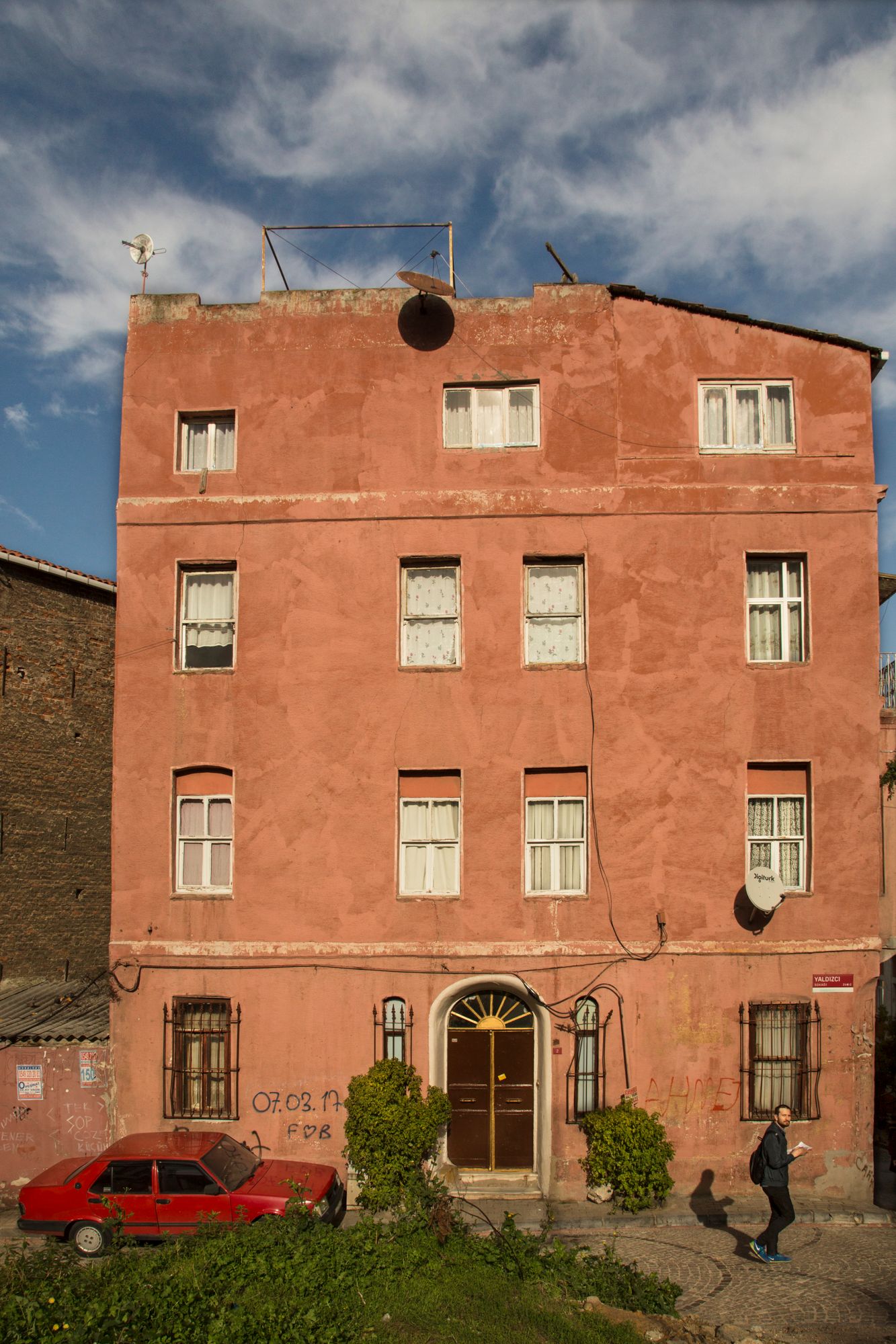 Four-story terracotta colored apartment building with classic architecture and small red car parked outside.