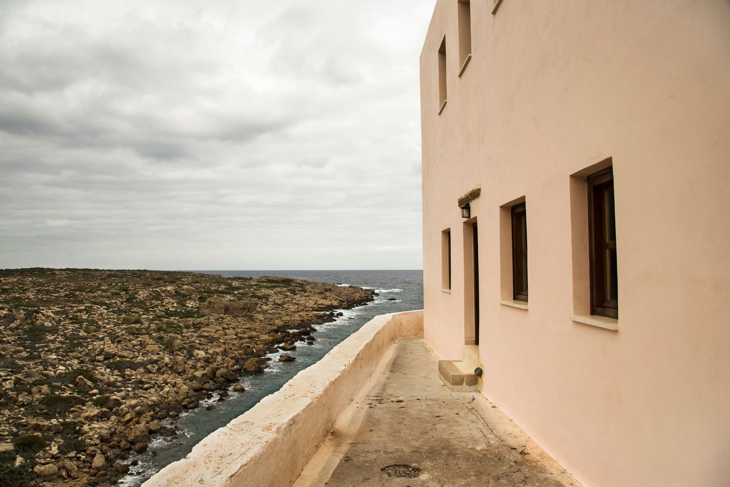 Beige building walls frame a coastal view over Mediterranean waters.