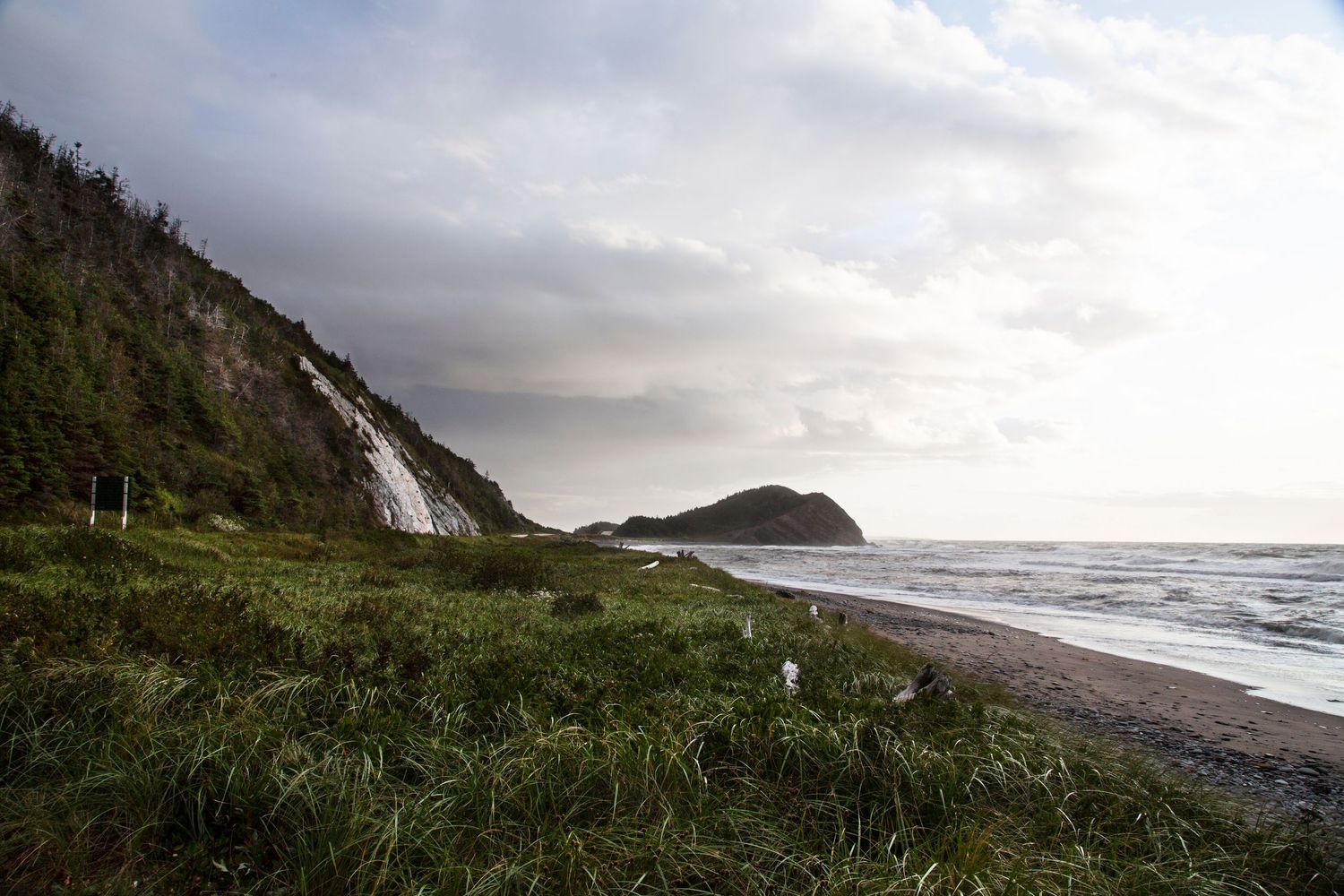 Dramatic coastline with waterfall cascading down cliff face near rocky beach at sunset.