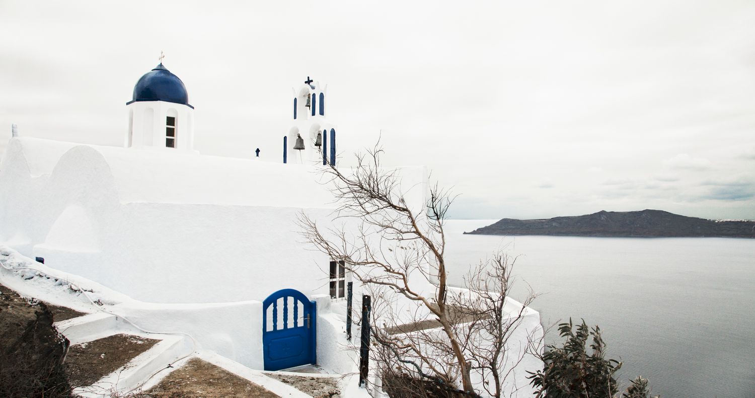 Traditional white Greek church with blue dome overlooking the sea.