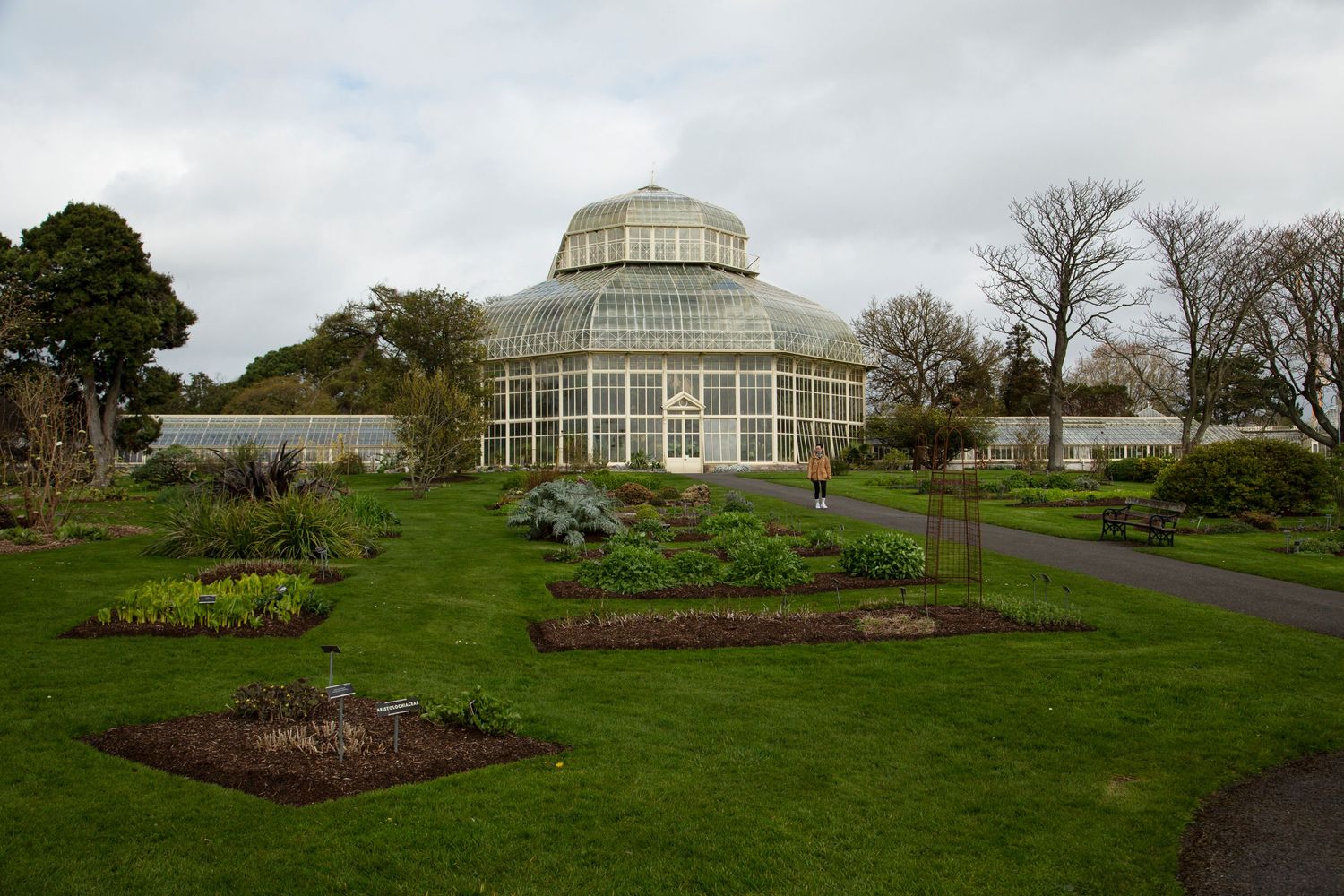 Panoramic view of a Victorian-style greenhouse building in a lush garden setting.