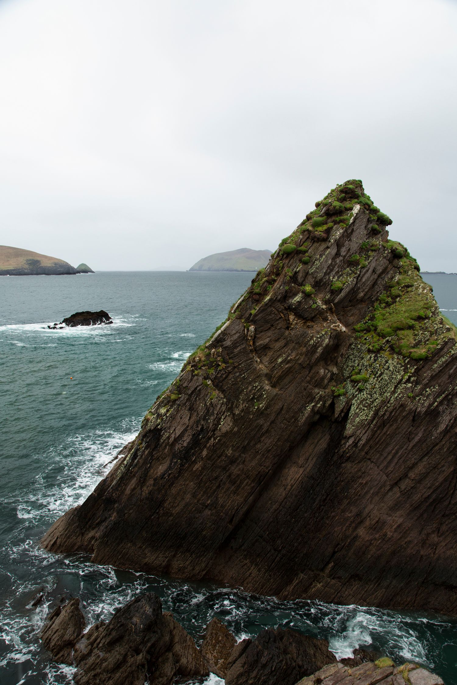 Jagged rock formations jut out into the turbulent sea with moss-covered surfaces.