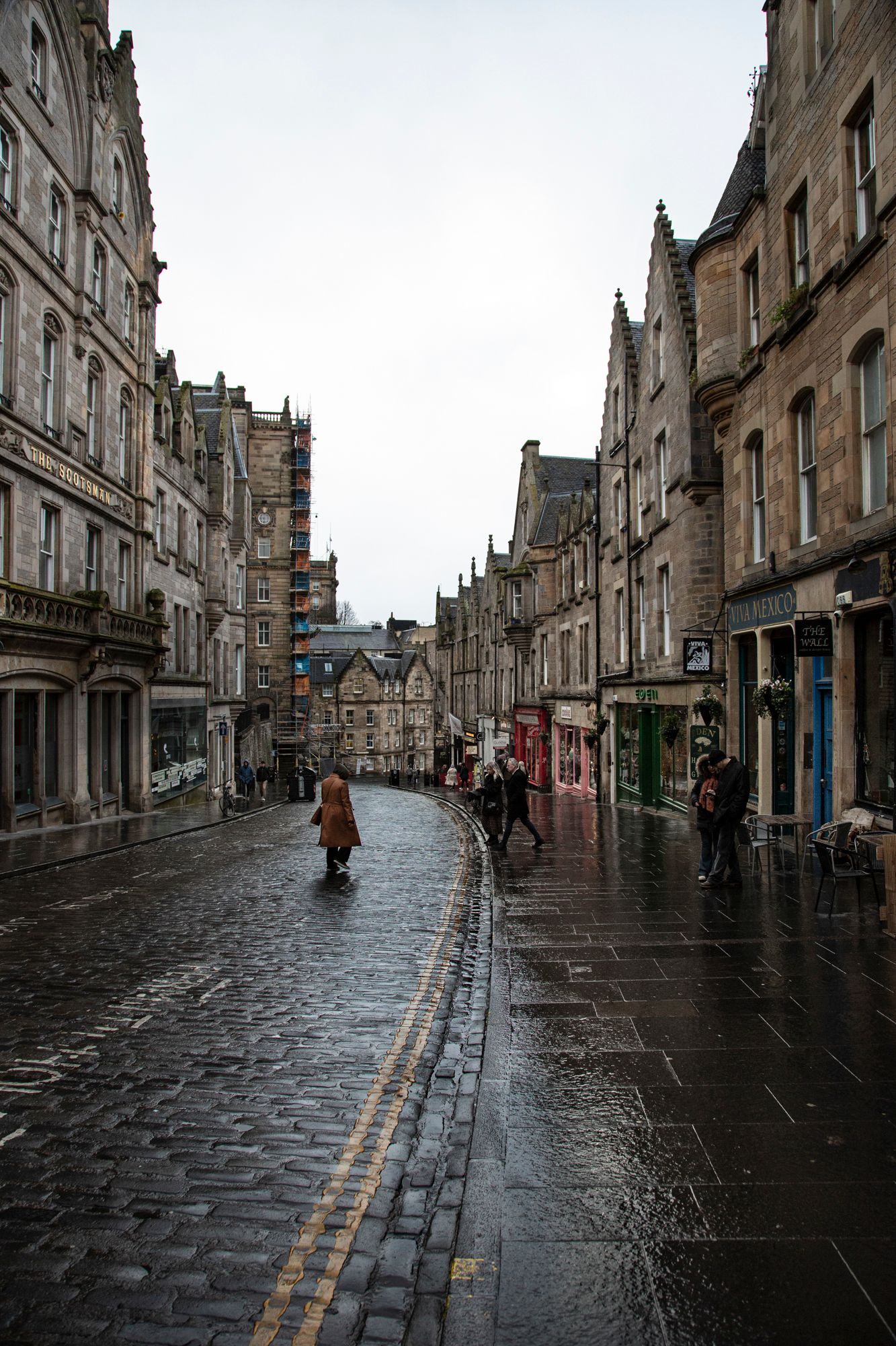 Wet cobblestone street in Edinburgh's historic Royal Mile with traditional Scottish architecture and shops on a rainy day.