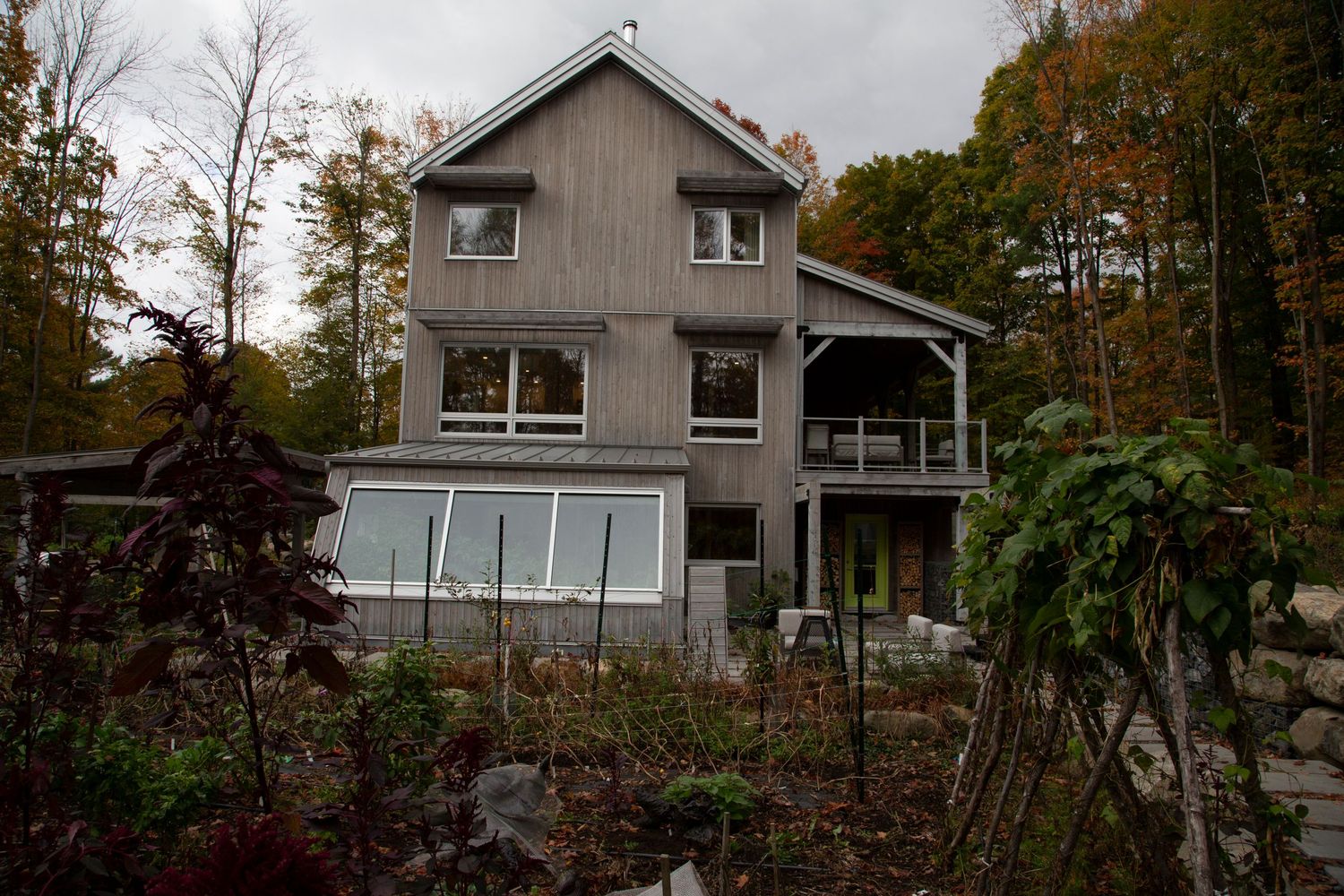 Contemporary gray house with large windows set among autumn trees on a wooded lot.