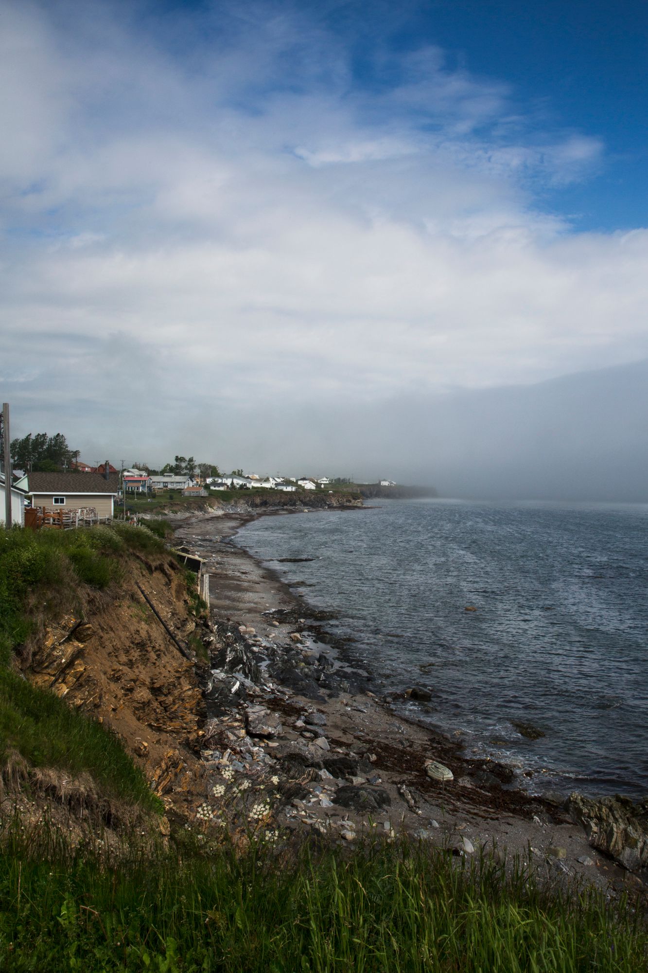 Rocky coastal shoreline with houses perched along cliffs under a dramatic cloudy sky.