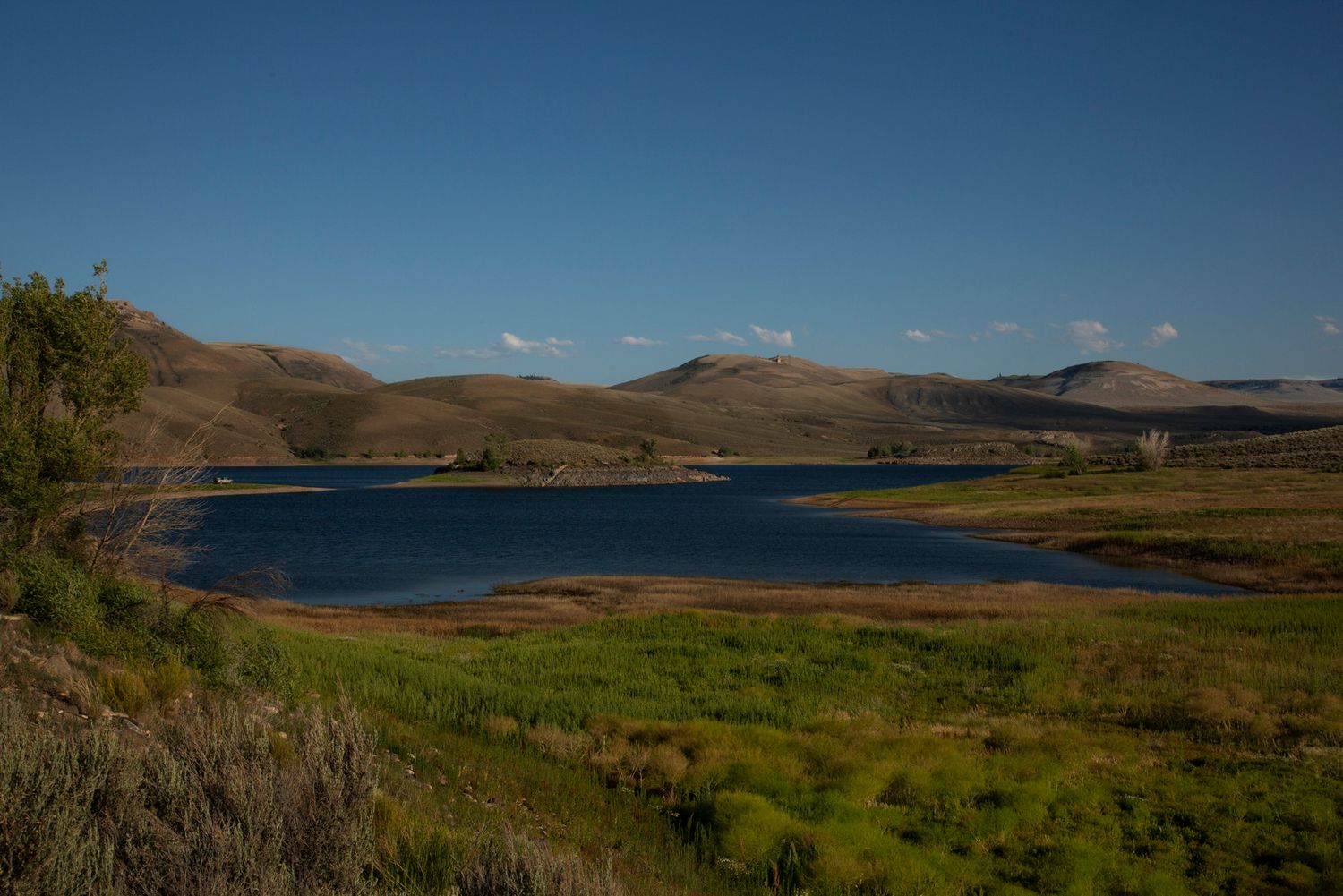 Scenic panoramic view of rolling green hills and a blue lake under clear skies in a mountainous landscape.