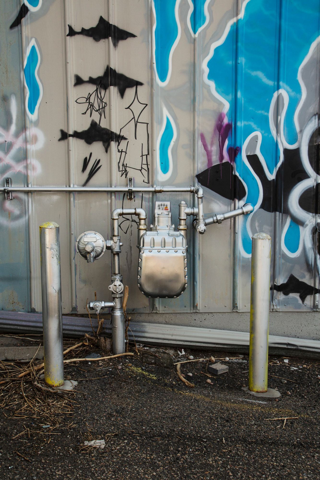 Street art mural featuring blue flames and black bats against a gray wall with metal poles in the foreground.