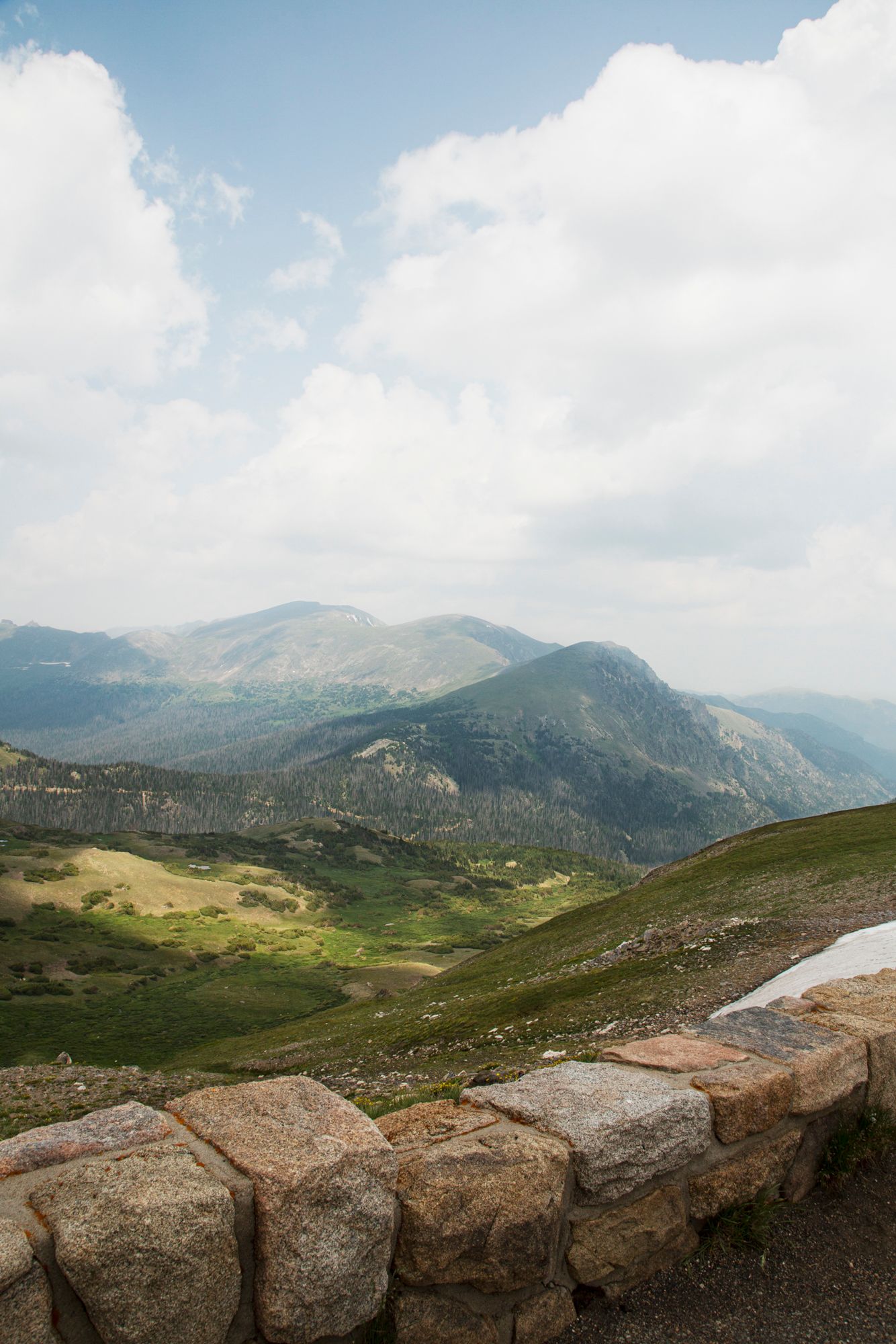 Mountain landscape with stone wall overlook featuring rolling hills, cloudy skies, and distant peaks in natural light.