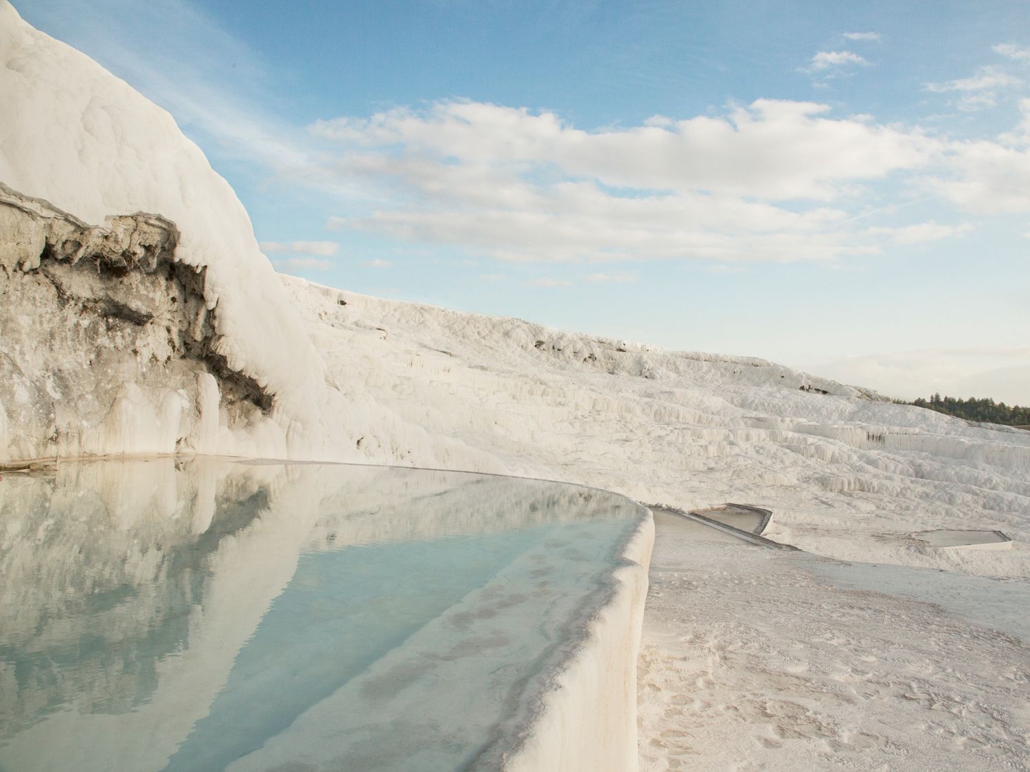 White travertine terraces with milky blue thermal water pools in Pamukkale, Turkey.