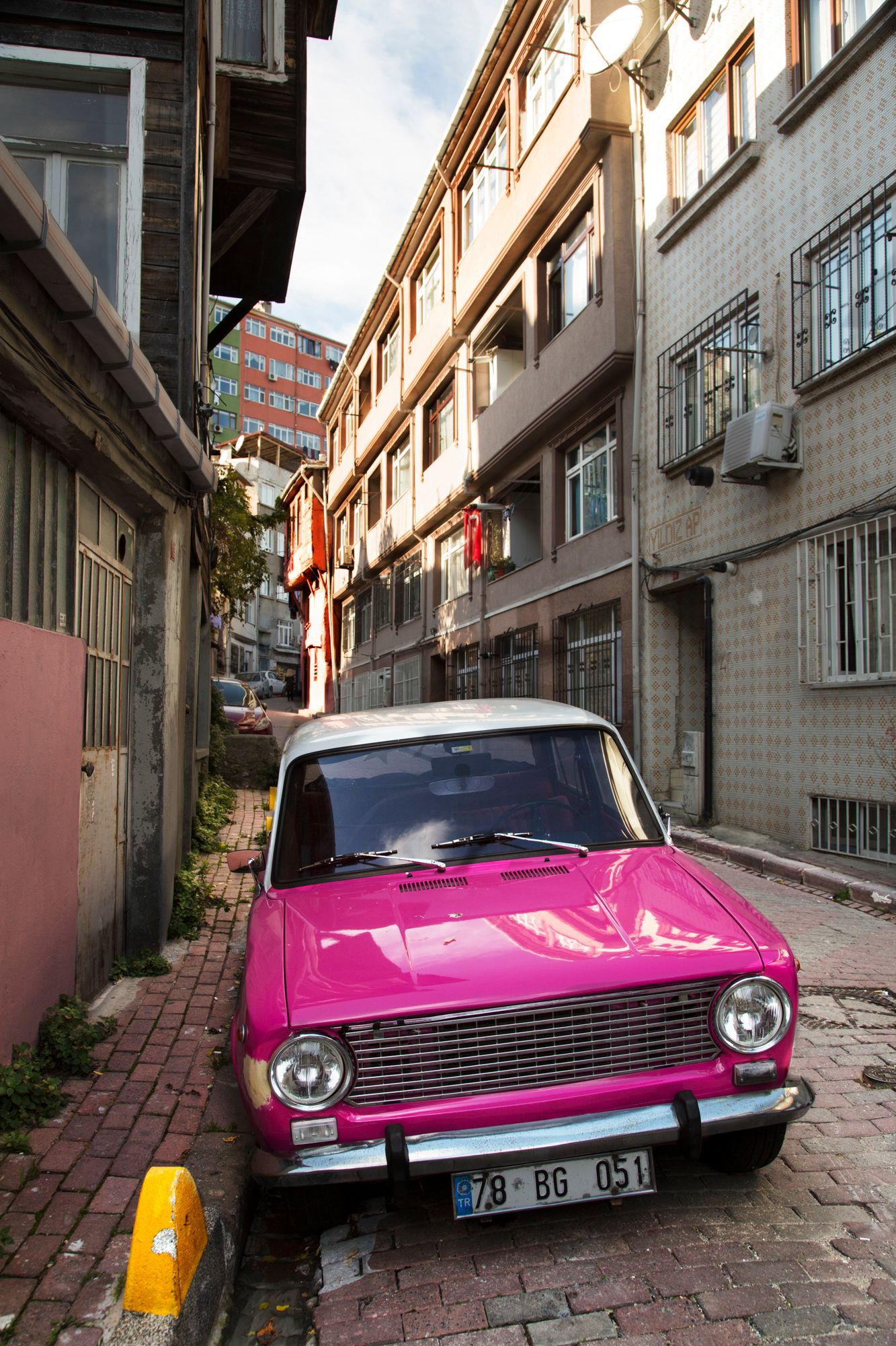 A bright pink vintage car parked on a narrow cobblestone street between old buildings.