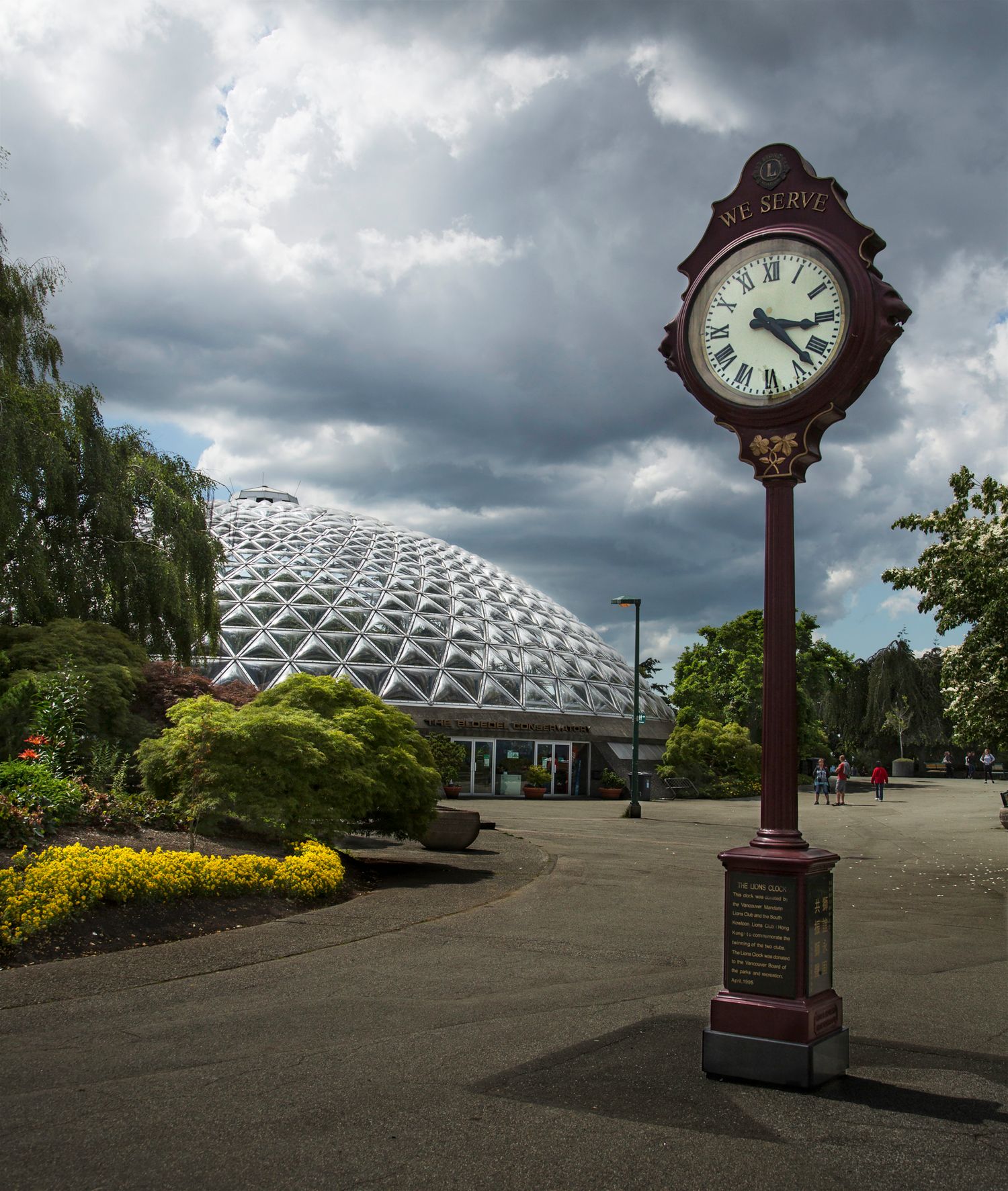 Modern geodesic dome structure and ornate clock post under stormy skies.