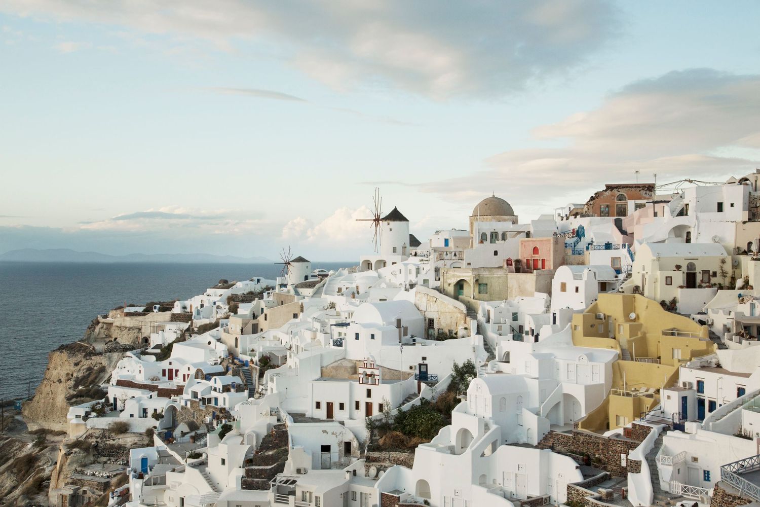 Sunset view of white Santorini buildings perched along coastal cliffs overlooking the Aegean Sea.