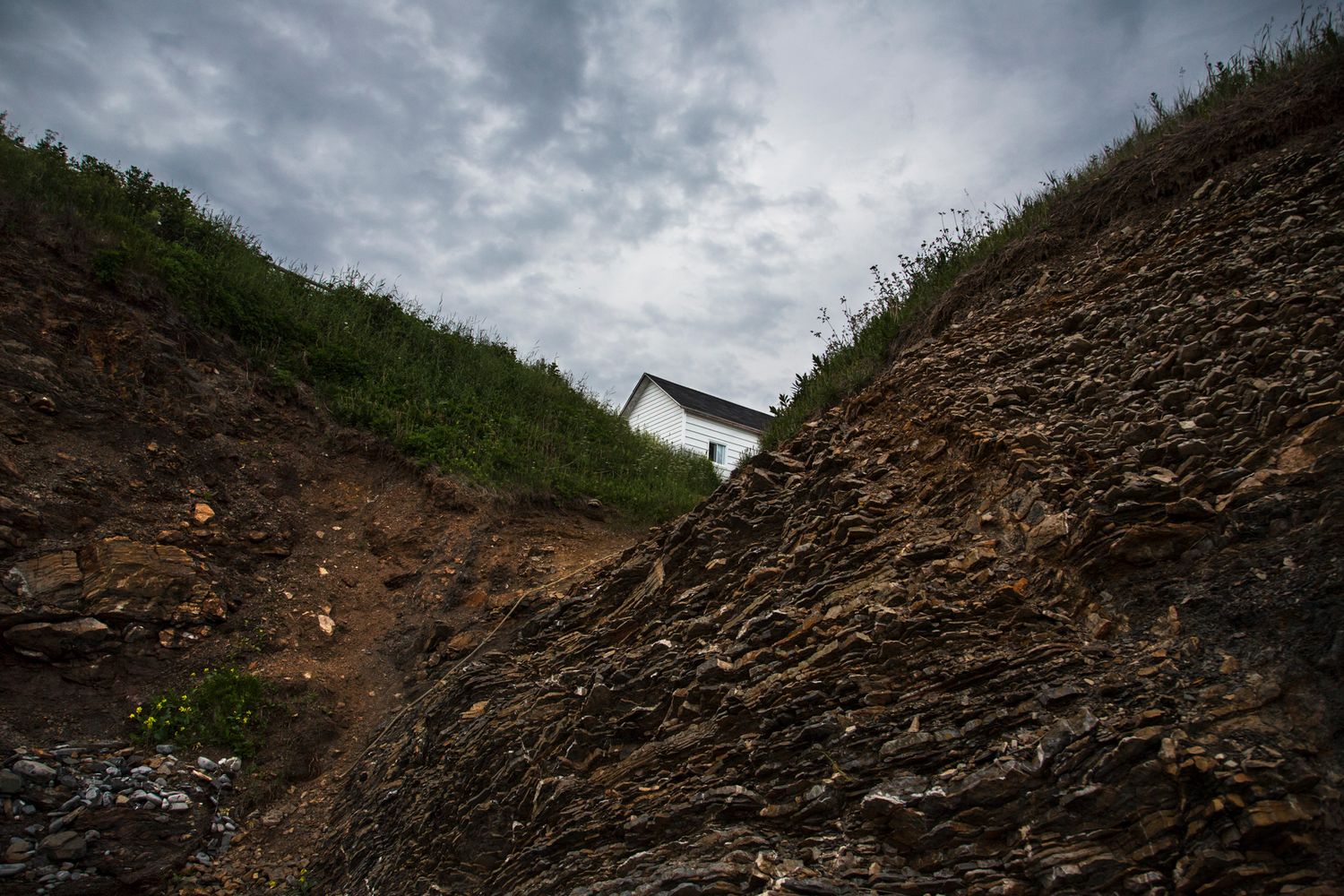 Rocky hillside with grass on top under dramatic cloudy sky.