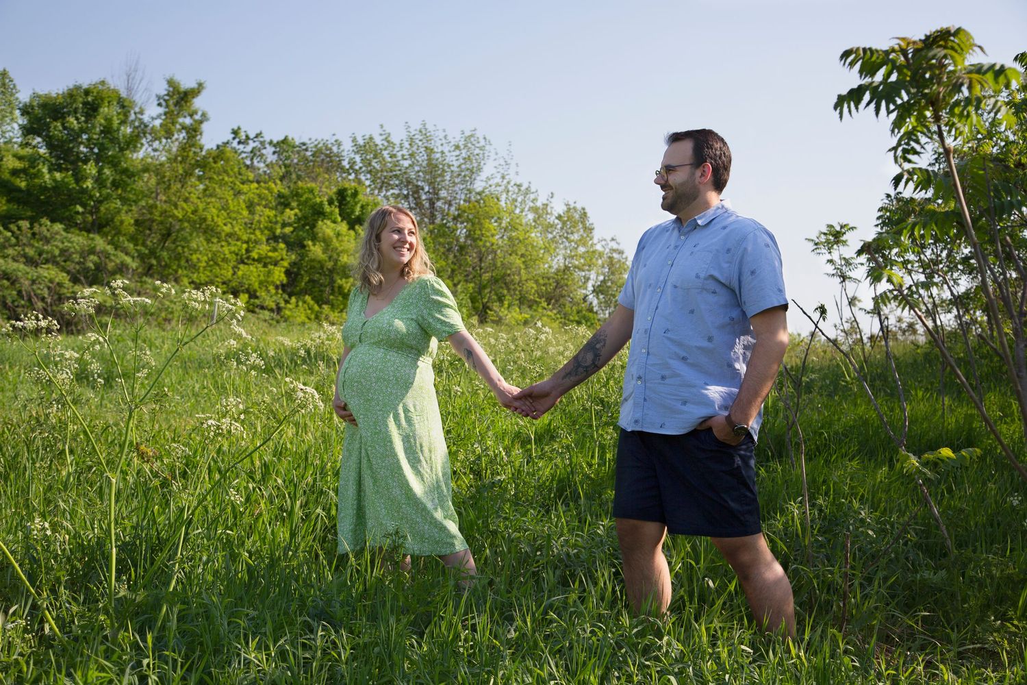 Playful outdoor maternity photo sequence of couple in casual clothes on grassy field.